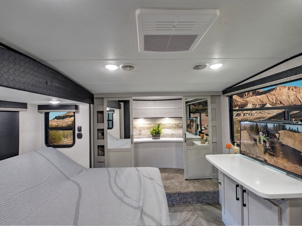 Spacious RV rental bedroom with a large bed, TV displaying off-road action, and stunning desert views from the windows.. Heartland Cyclone 2021