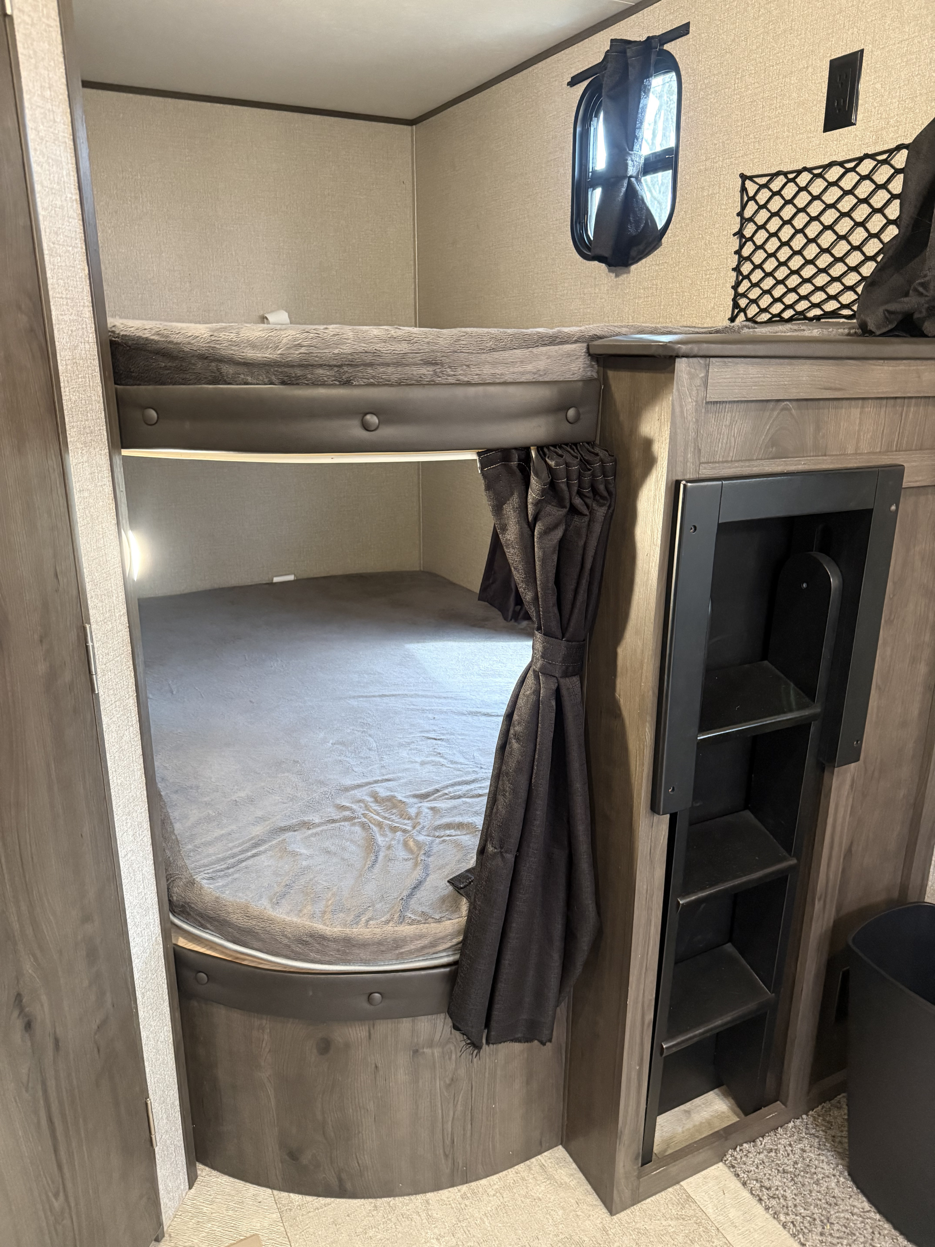 Inside an RV rental: modern bunk beds with gray bedding, a privacy curtain, window, & storage for compact travel.. Jayco Jay Flight 2020