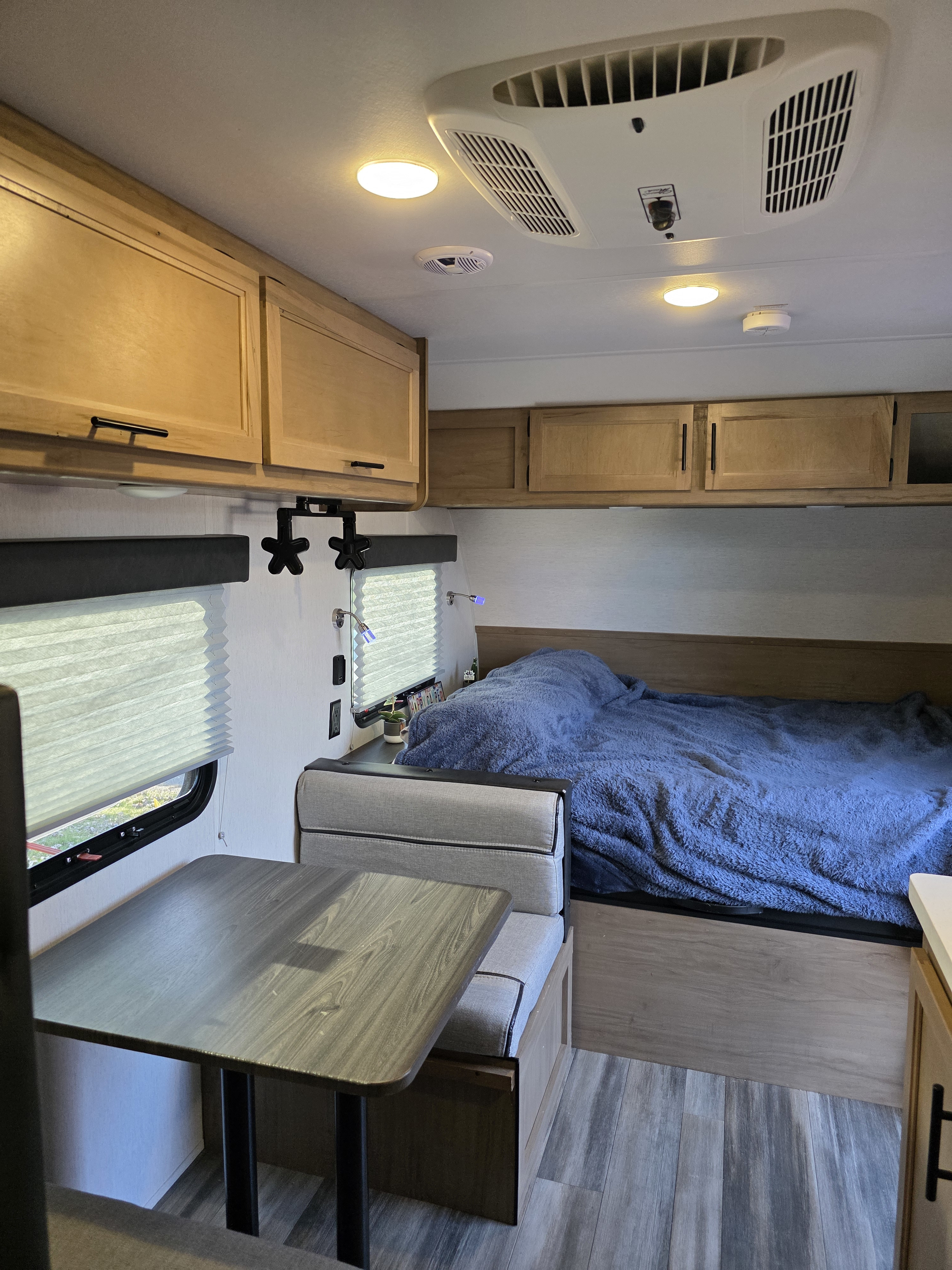 Inside an rv rental: a comfy bed with a blue blanket, a dinette, storage cabinets, and bright lighting in a compact living space.. Forest River Cherokee Wolf Pup 2023