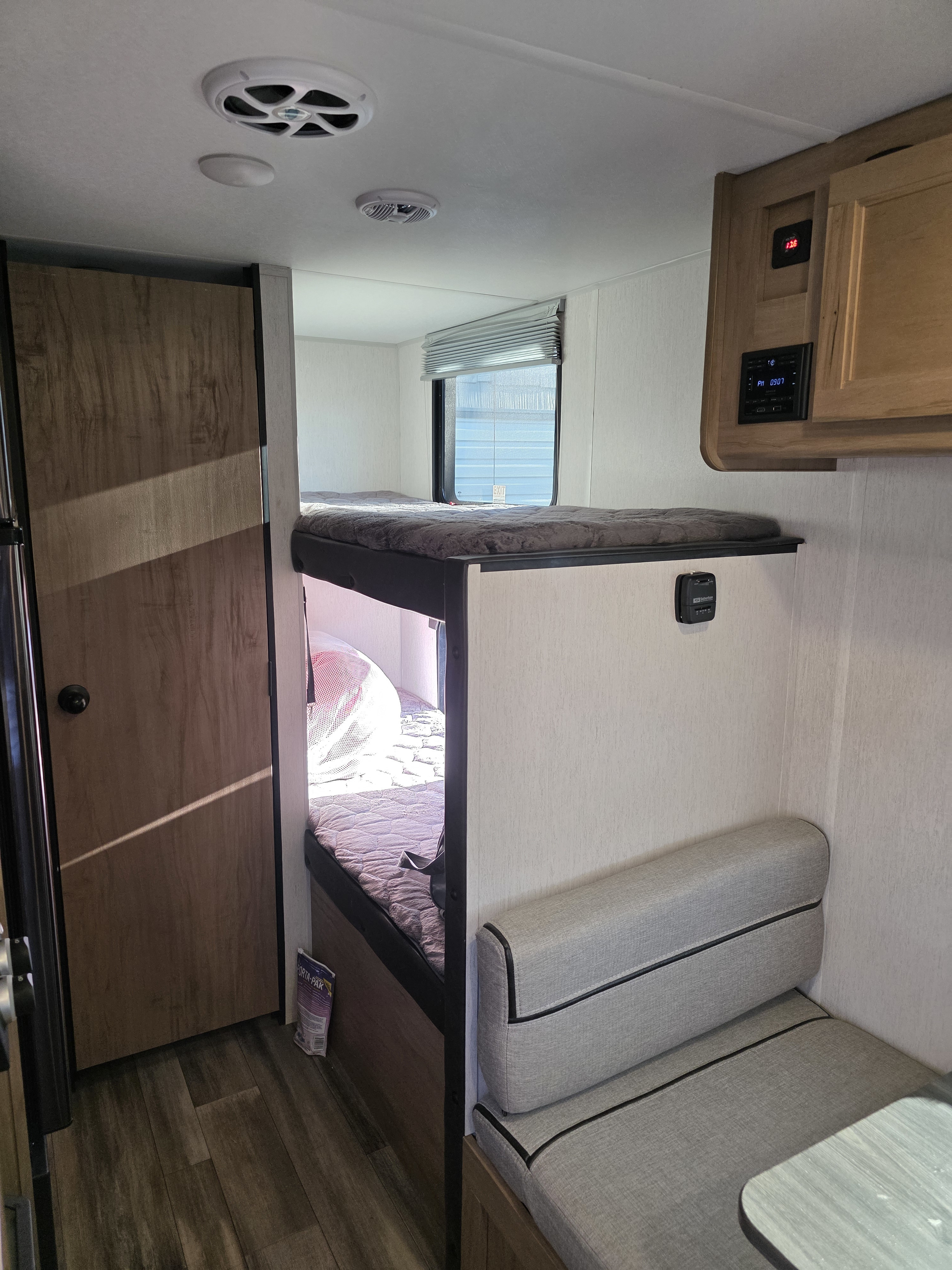 Inside this RV rental: comfortable bunk beds, a gray dinette bench, ceiling speaker, thermostat, and wood-look flooring.. Forest River Cherokee Wolf Pup 2023