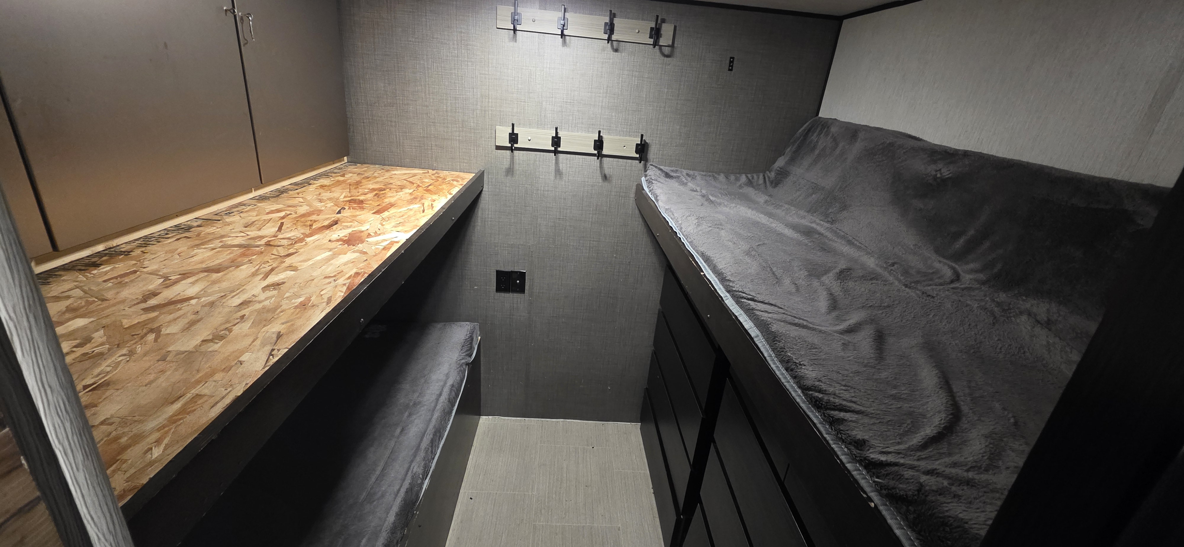 This RV rental bunk room features two bunk beds; one with an OSB base, the other ready with a gray blanket. Hooks and outlets are visible.. Heartland RVs Prowler 2020
