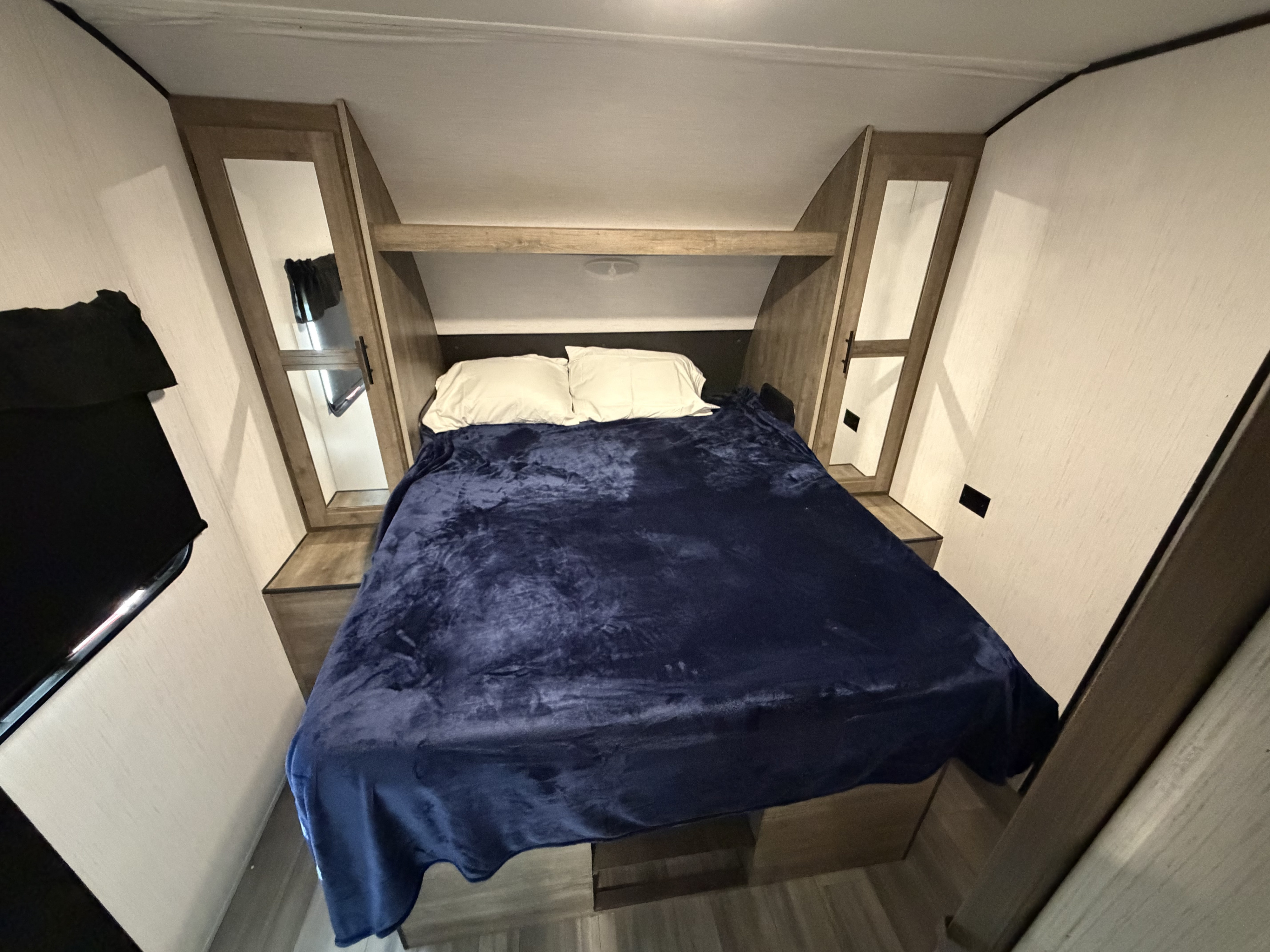 Cozy RV rental bedroom featuring a large bed with a blue blanket, white pillows, and practical built-in storage units.. Heartland RVs Pioneer 2021