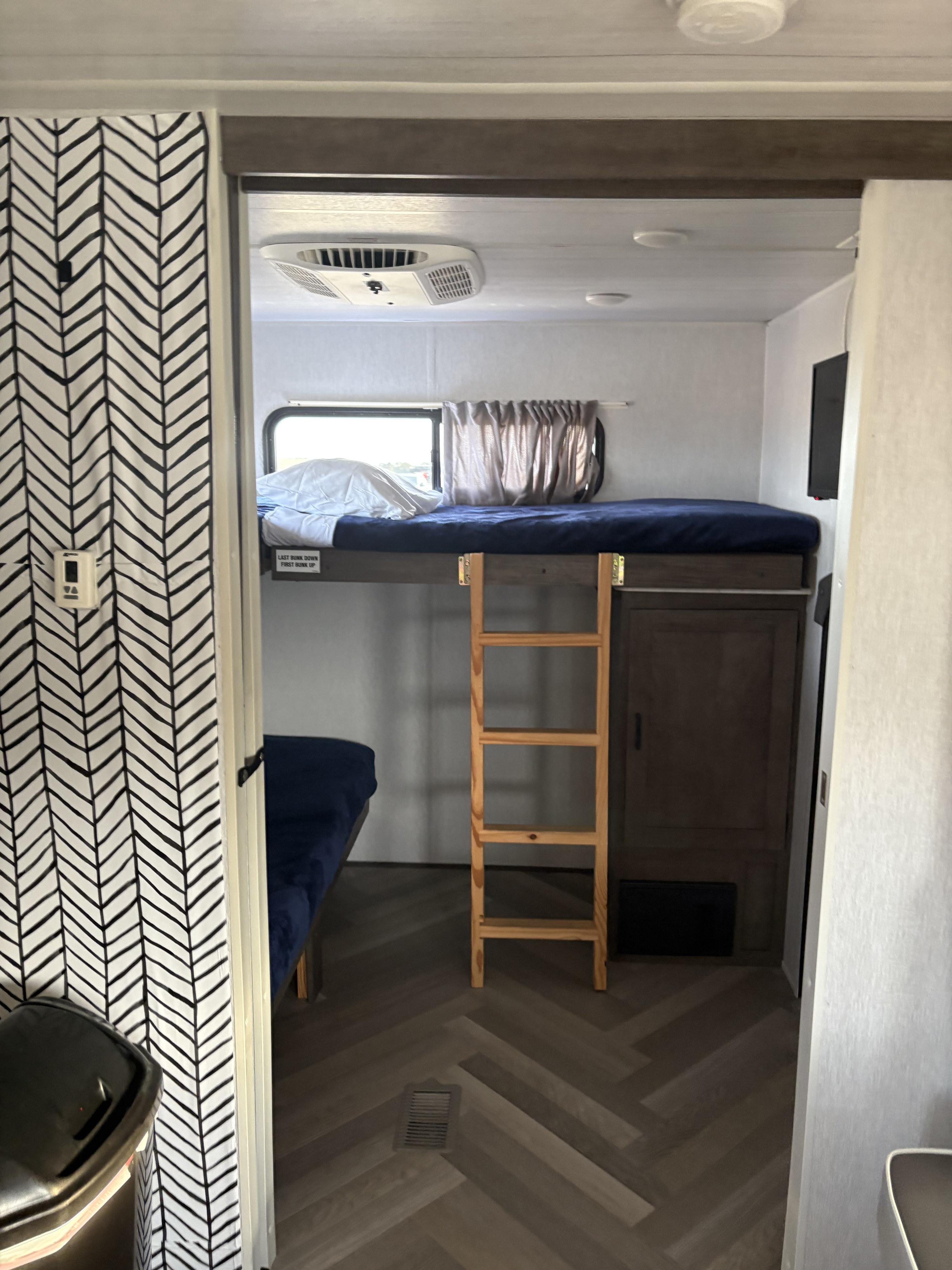Inside this RV rental, a bunk bed area features a wooden ladder, window, and a stylish black and white chevron-patterned wall.. Forest River Wildwood 2022