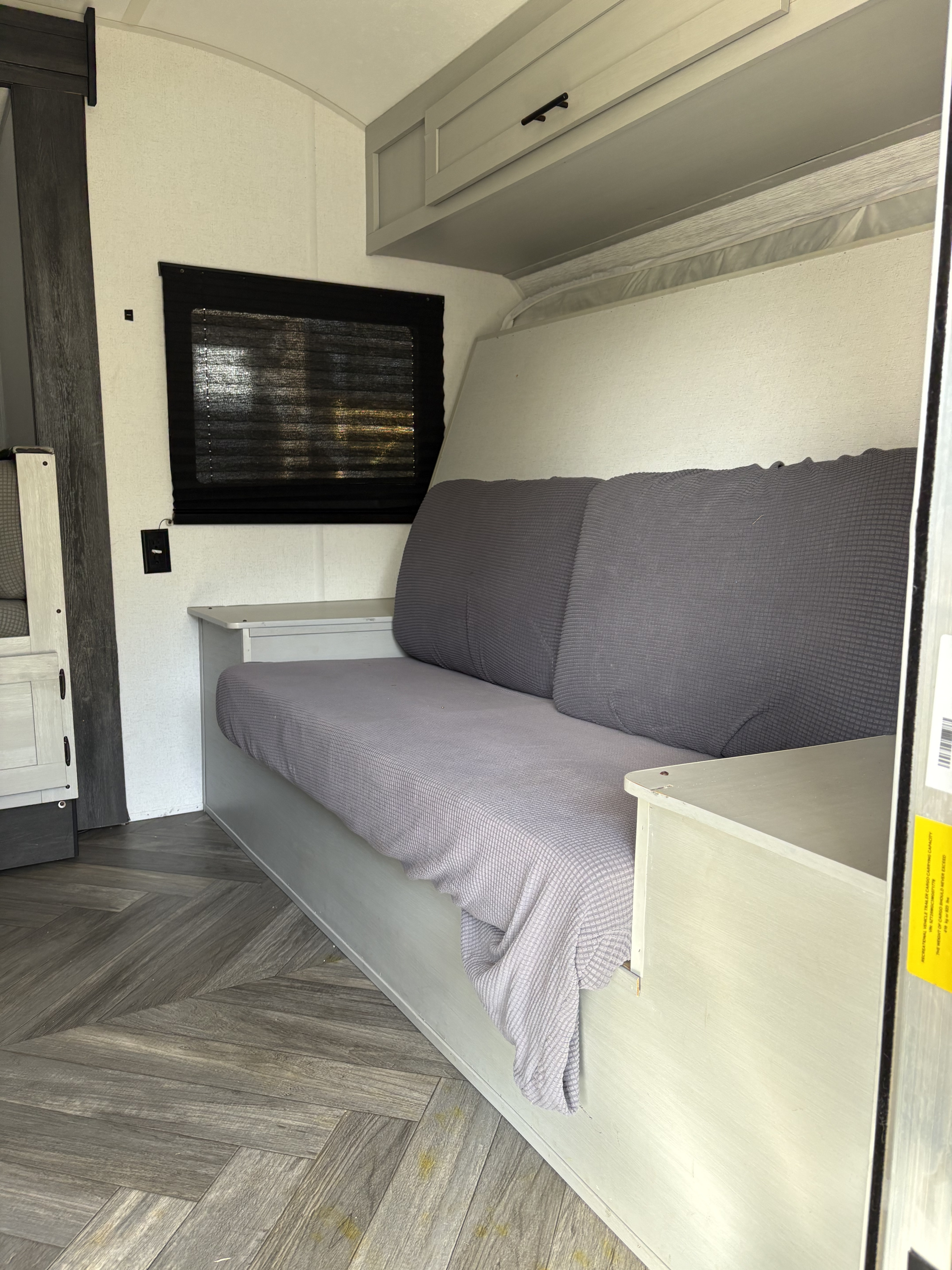 Cozy RV rental interior featuring a comfy grey daybed, practical overhead storage, and stylish wood-look floor for your travels.. Forest River Salem FSX 2021