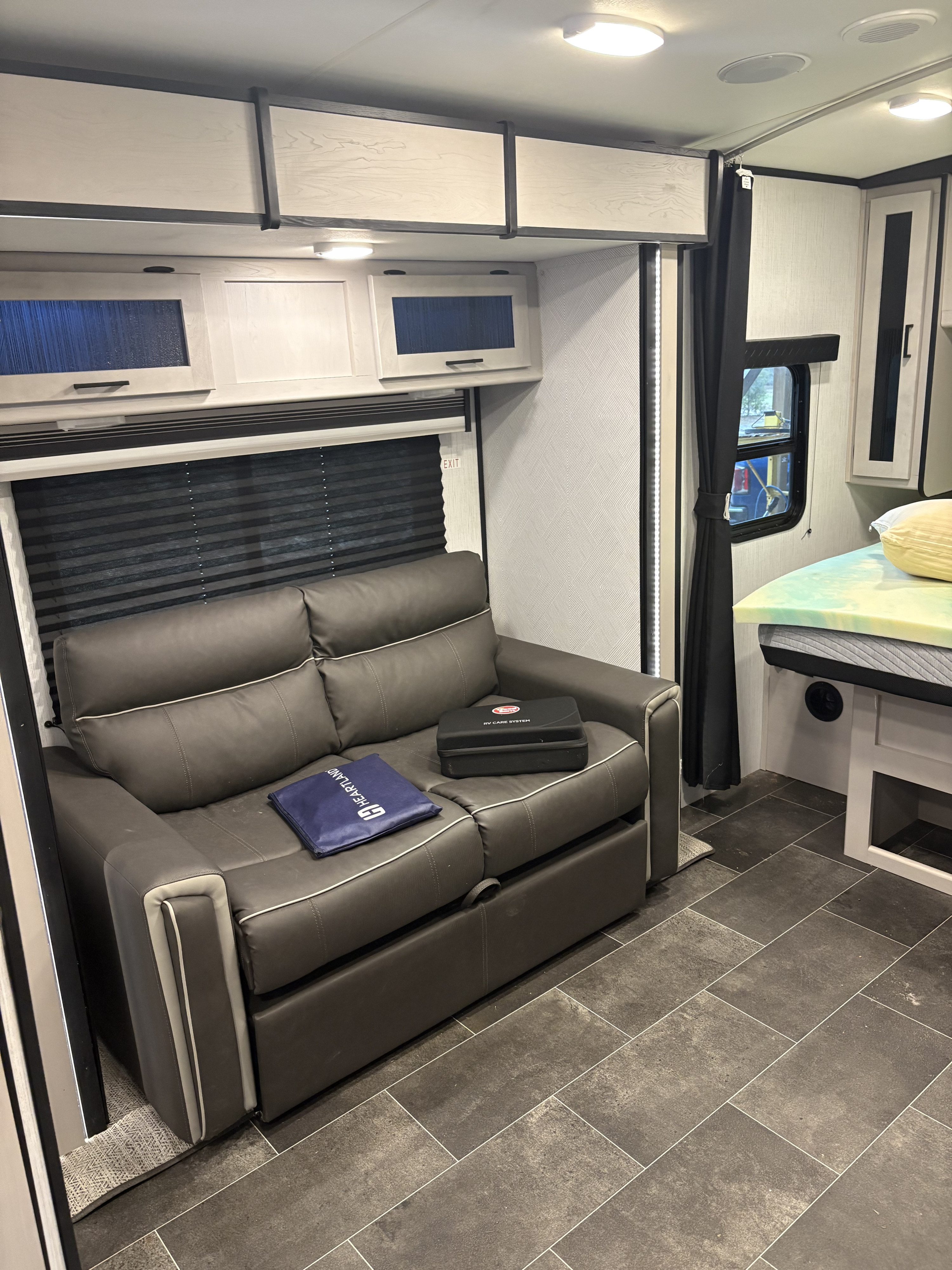 RV rental interior: modern living area with a dark sofa, light cabinets, and a bed. Perfect for your next trip.. Heartland RVs Mallard 2022