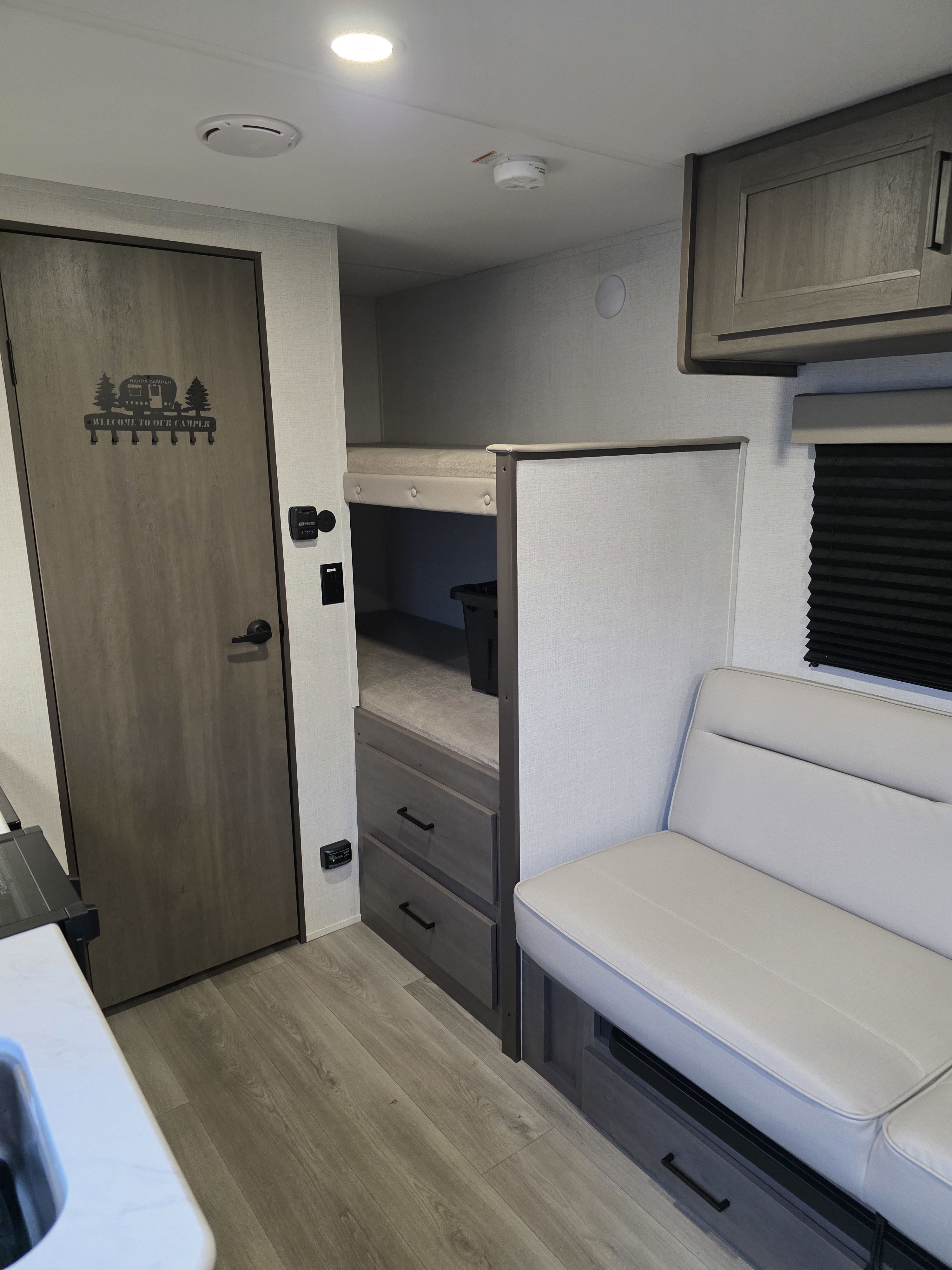 RV rental interior showcasing compact bunk beds, a comfy dinette with storage, and a welcoming door with key hooks.. Grand Design Transcend One 2025