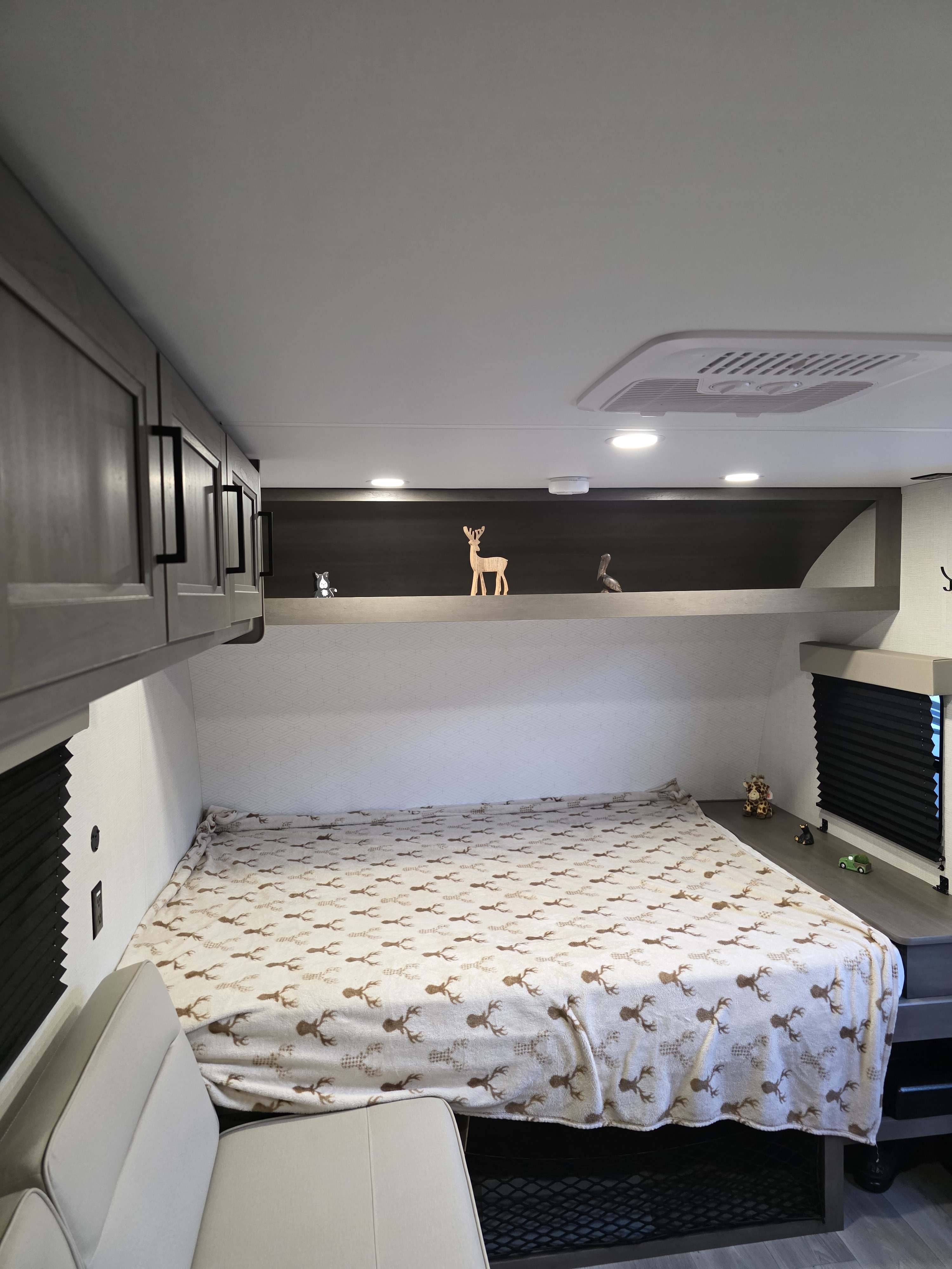 Inside a comfortable RV rental bedroom, featuring a bed with deer print blanket, storage, and decorative shelf with figurines.. Grand Design Transcend One 2025