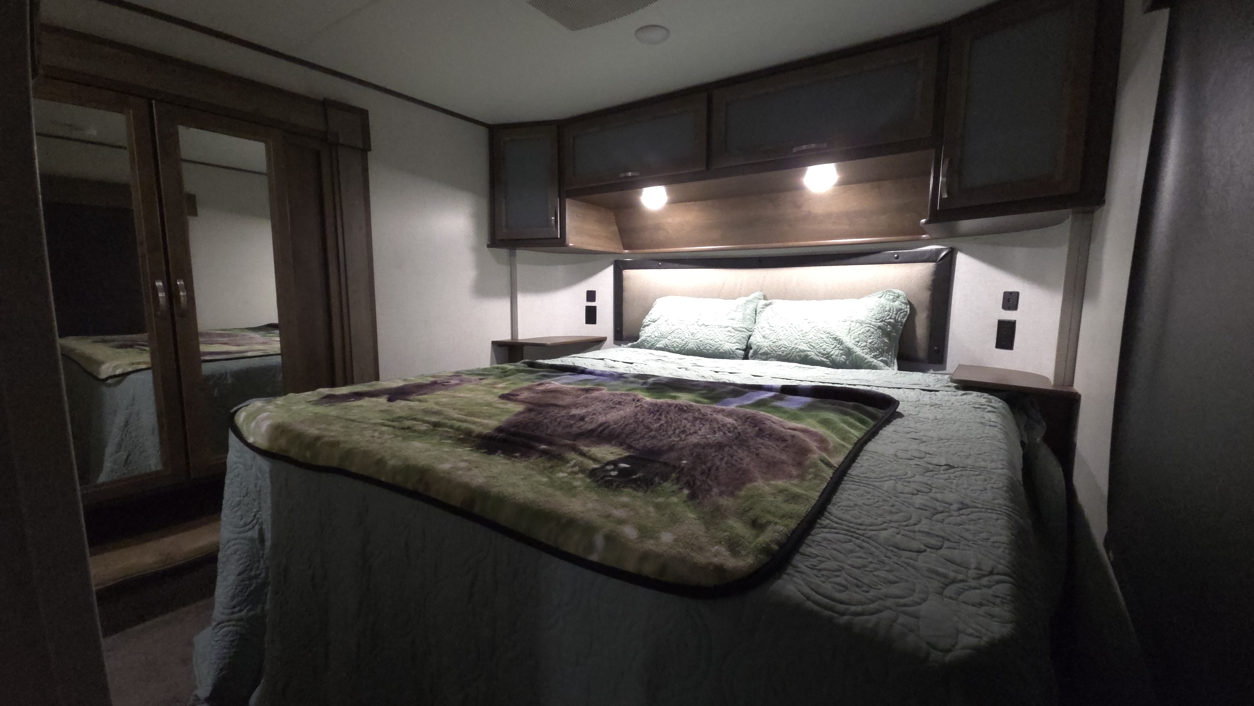 Cozy RV rental bedroom featuring a large bed with an animal-print blanket, lighted overhead cabinets, and mirrored closet doors.. Highland Ridge RV Highlander Toy Hauler 2019