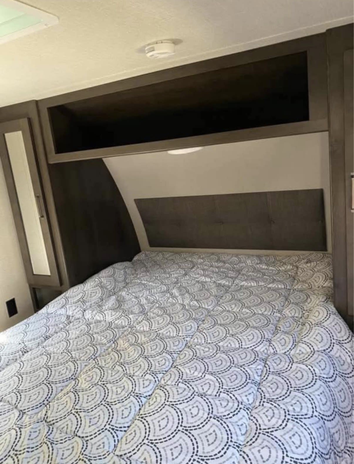 An rv rental bedroom features a patterned bed, dark wood headboard, overhead cabinets, and a side wardrobe.. Grand Design Transcend Xplor 2021