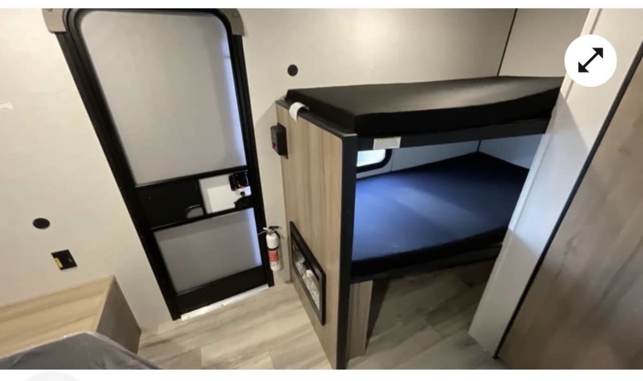 RV rental interior: view of compact bunk beds with dark mattresses, an entrance door, and a fire extinguisher.. Keystone RV Coleman 13B 2026