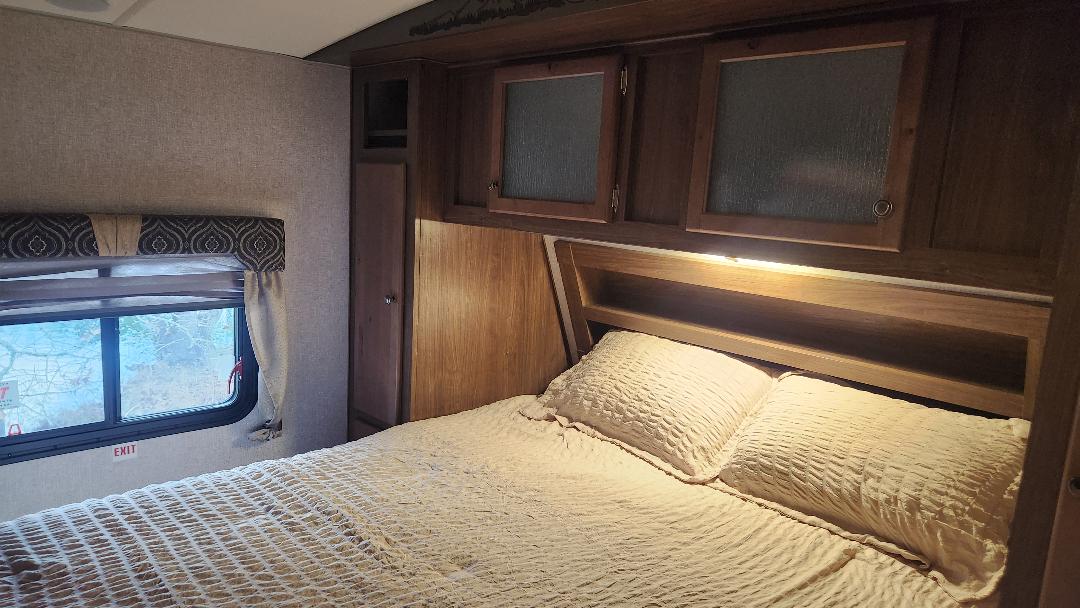 Cozy RV rental bedroom features a bed, overhead cabinets, a window with an exit sign. Ideal for travel comfort.. Nash Nash Trailer 2021