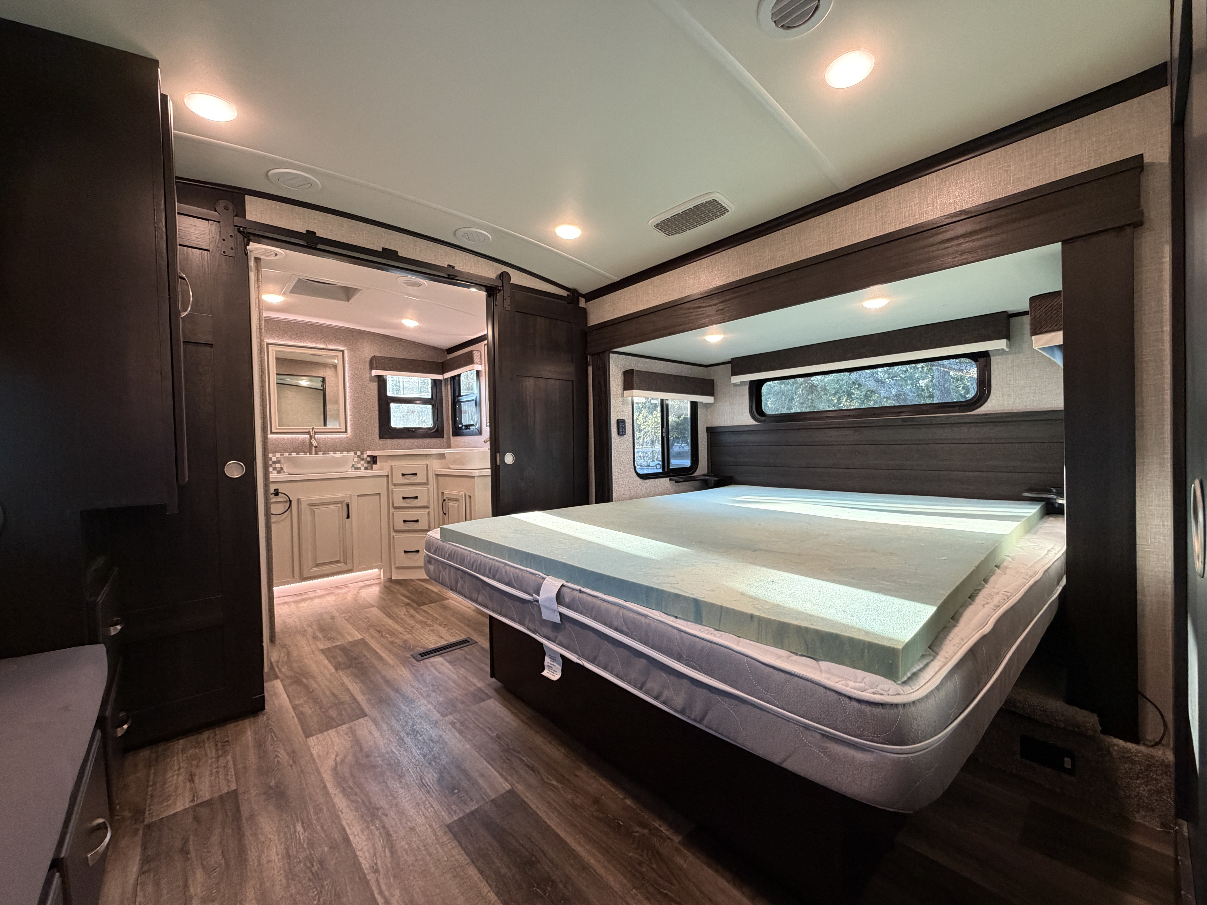 Experience comfort in this RV rental's bedroom, featuring a bed with a foam topper and an adjacent bathroom with dual sinks.. Jayco North Point 2022
