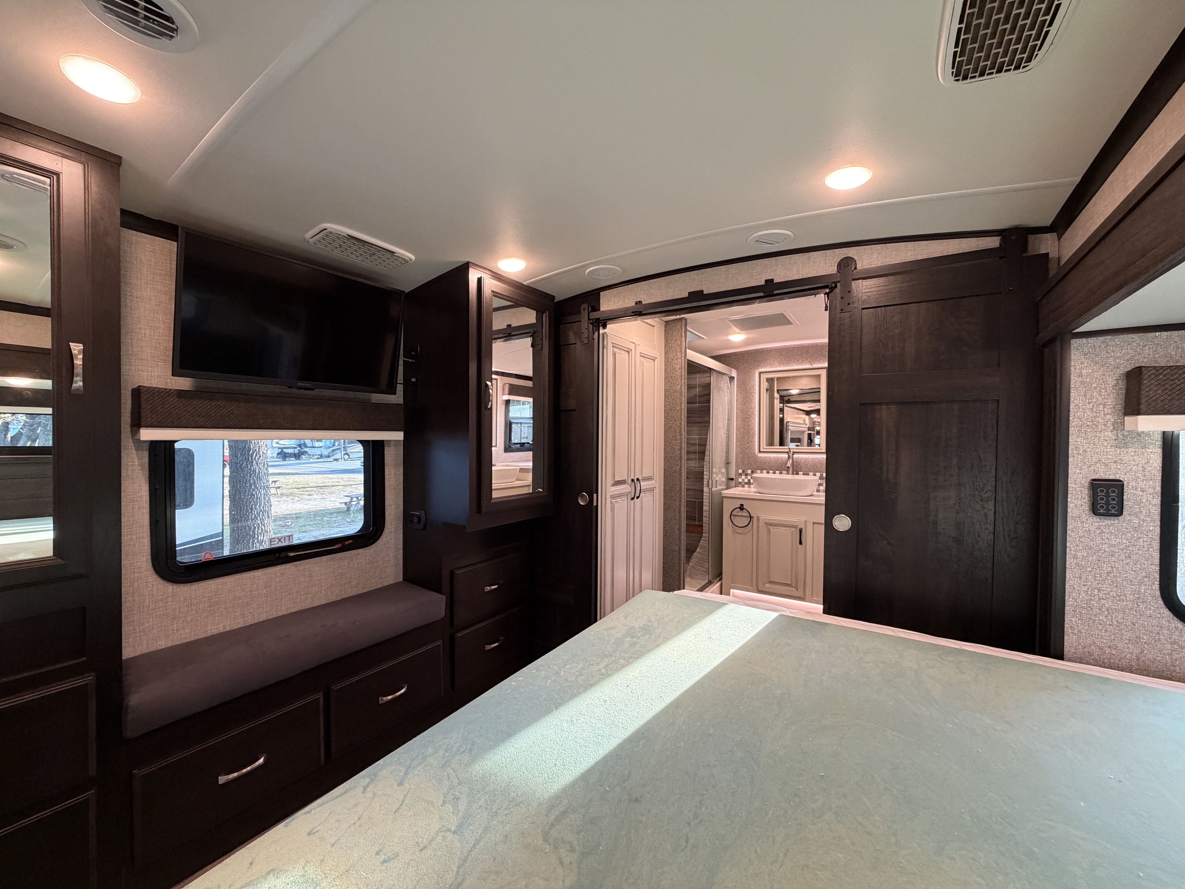 Modern RV rental bedroom with a connected bathroom, featuring dark wood accents, built-in TV, and ample storage.. Jayco North Point 2022
