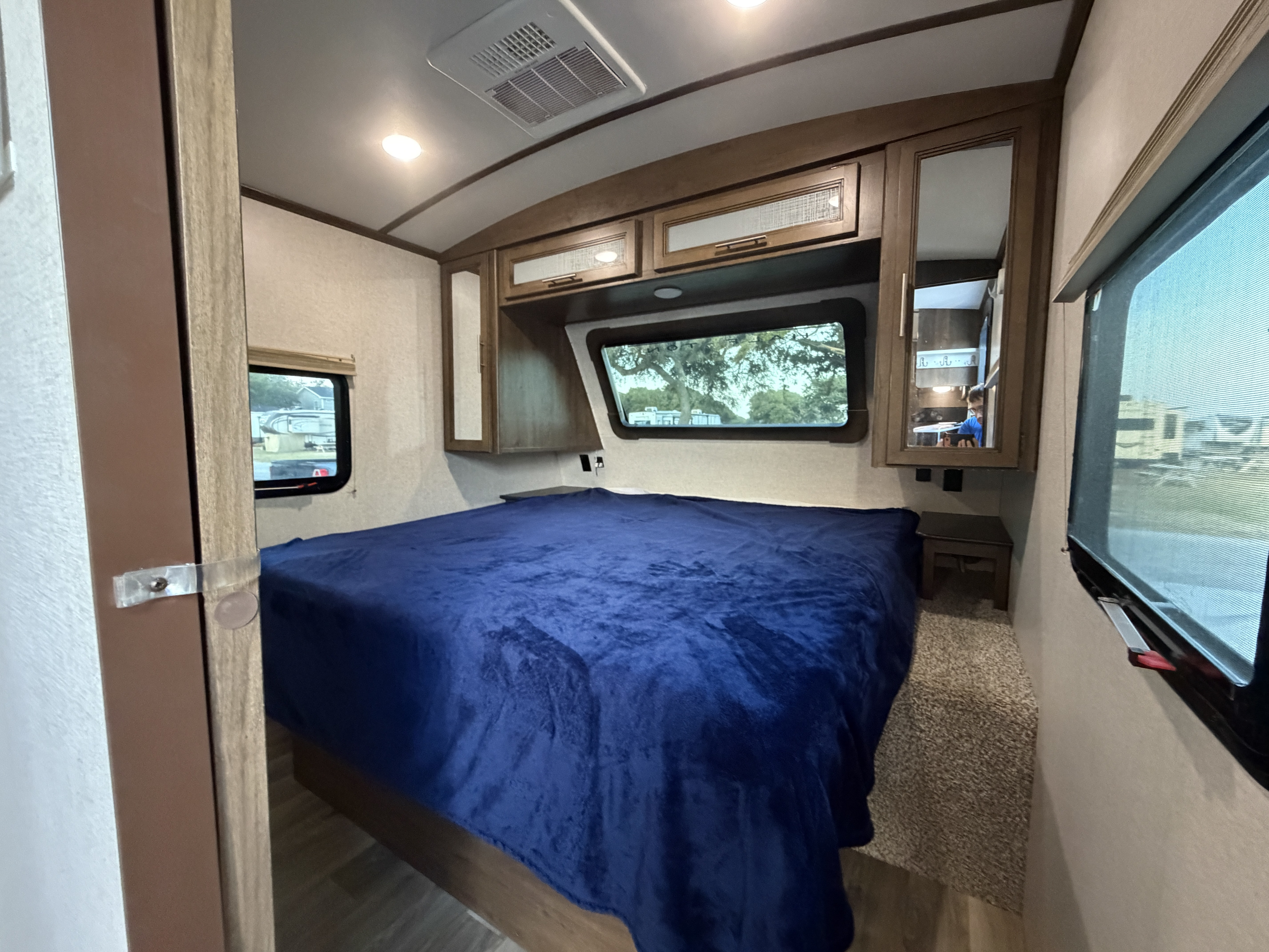 Inviting RV rental bedroom: large bed with blue blanket, overhead storage, side windows, and AC unit for comfort.. Keystone Cougar Half-Ton 2020