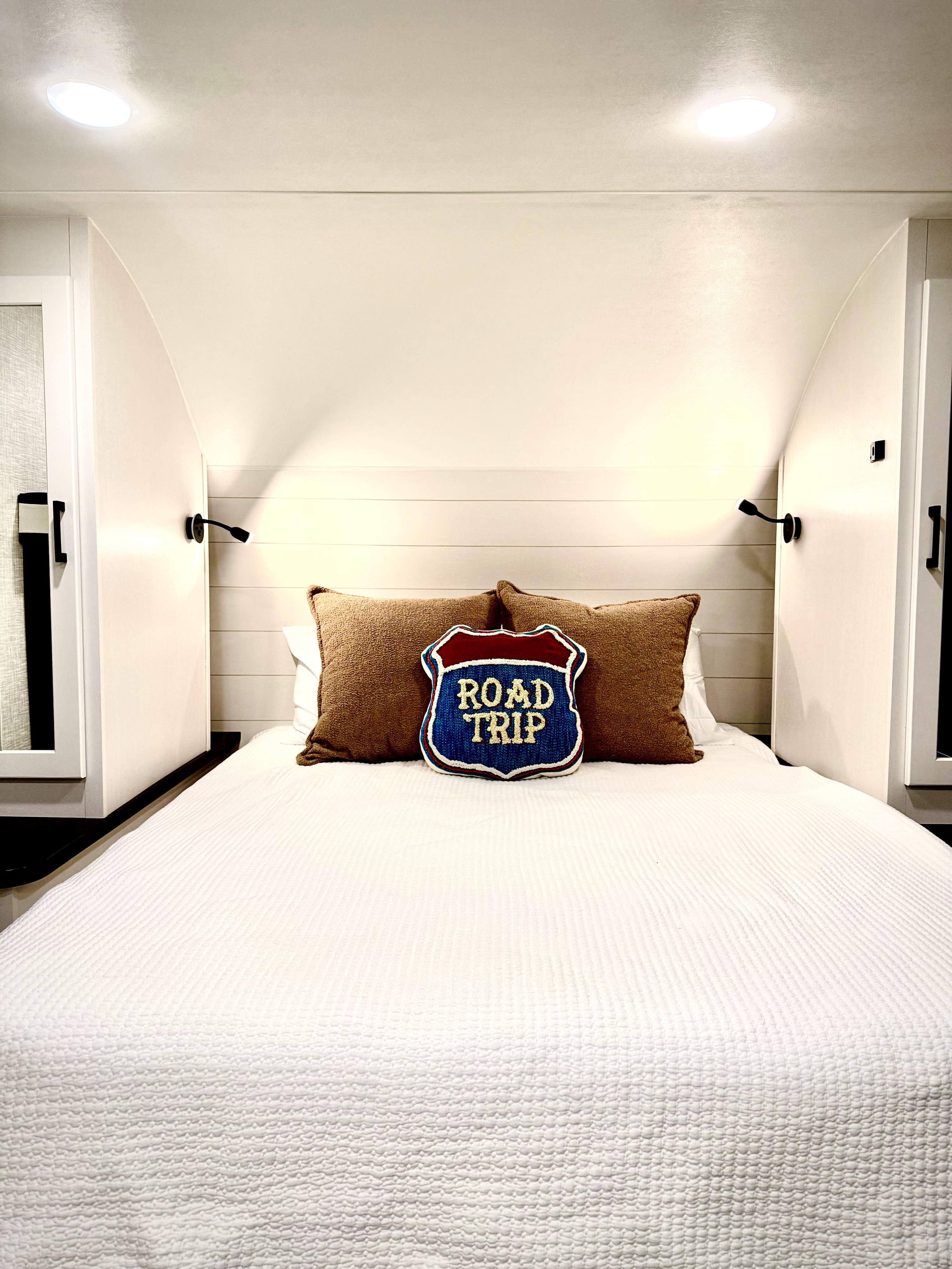 Inviting RV rental bedroom with a neatly made white bed, brown pillows, and a central "ROAD TRIP" decorative pillow.. Jayco Jay Feather Micro 2024