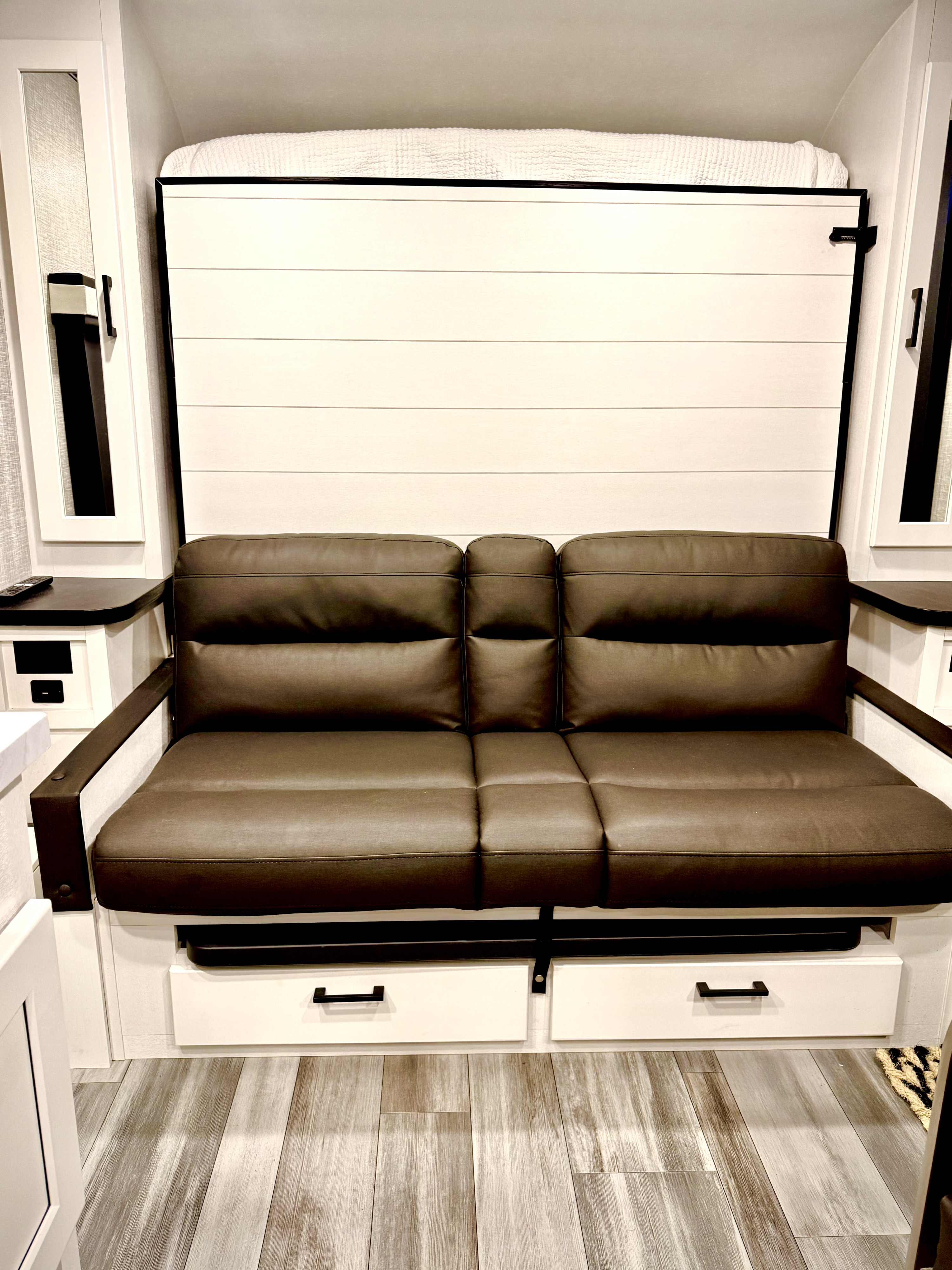 RV rental interior features a brown leather sofa below a folded murphy bed against a shiplap wall, maximizing space.. Jayco Jay Feather Micro 2024