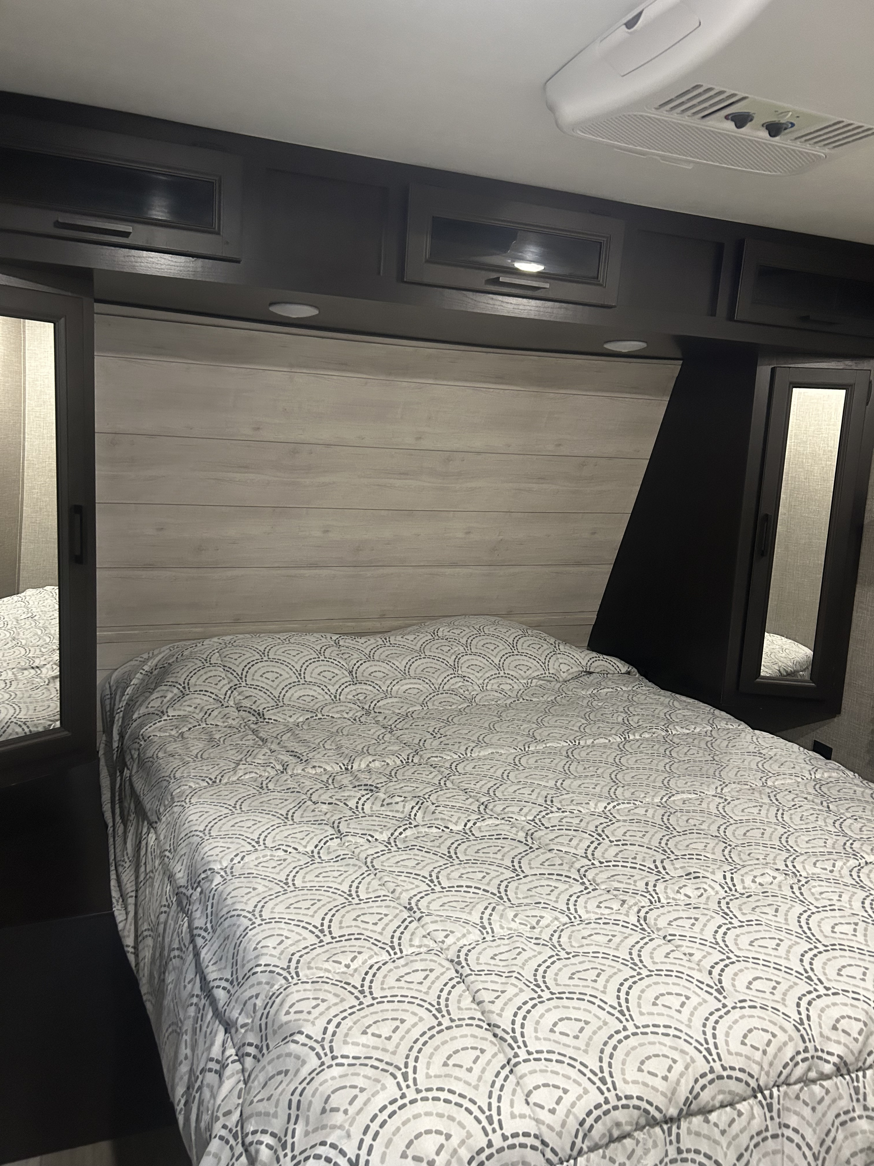 Experience a comfortable rv rental bedroom. Features include a patterned bedspread, wood-look headboard, and overhead cabinets.. Jayco Jay Flight 2022
