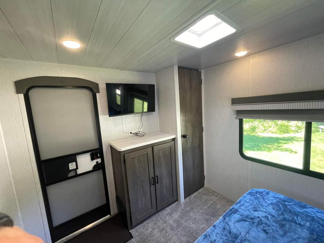 RV rental bedroom interior with wall-mounted TV, small cabinet, entrance door, and window. Comfortable travel space.. Wildwood 36VBDS 2022