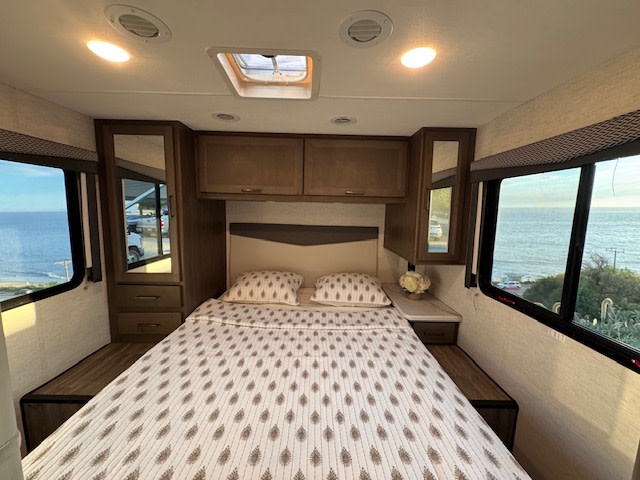 Experience a beautiful ocean view from this cozy RV rental bedroom, featuring a comfortable bed and ample storage.. Thor Four Winds 2025