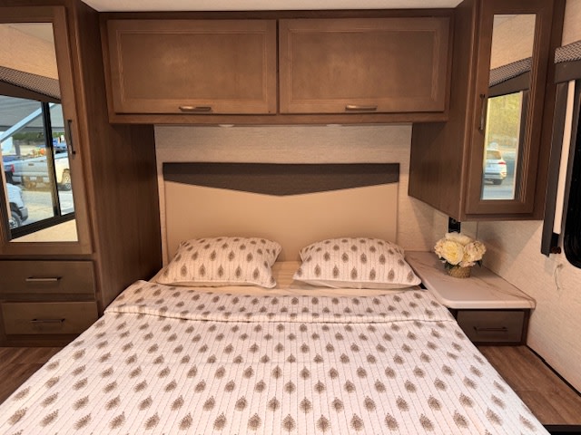 Cozy rv rental bedroom interior: bed with patterned quilt, overhead cabinets, and mirrored side storage for a comfortable travel stay.. Thor Four Winds 2025