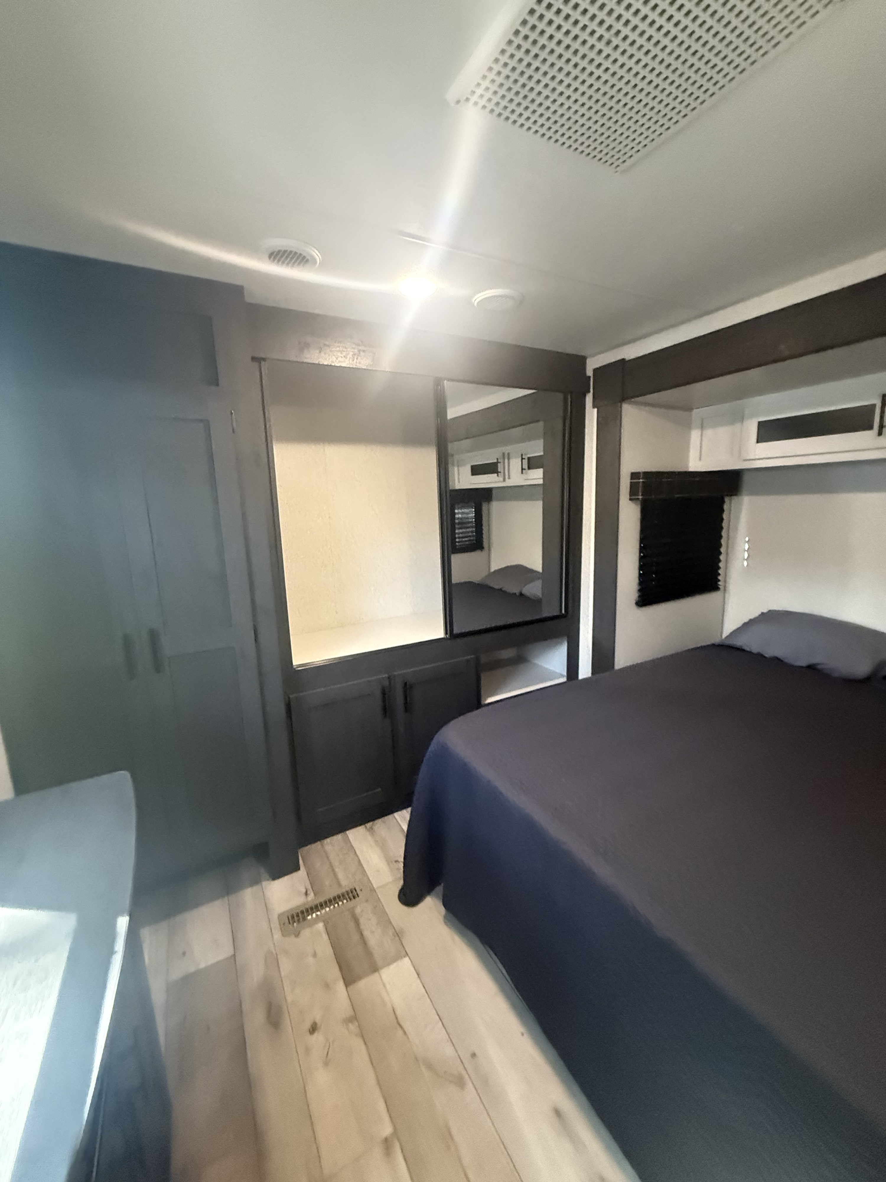 Cozy RV rental bedroom with dark bedding, a mirrored closet, wardrobe, wood-look floor, and ceiling vents.. KZ RV Sportsmen 2022
