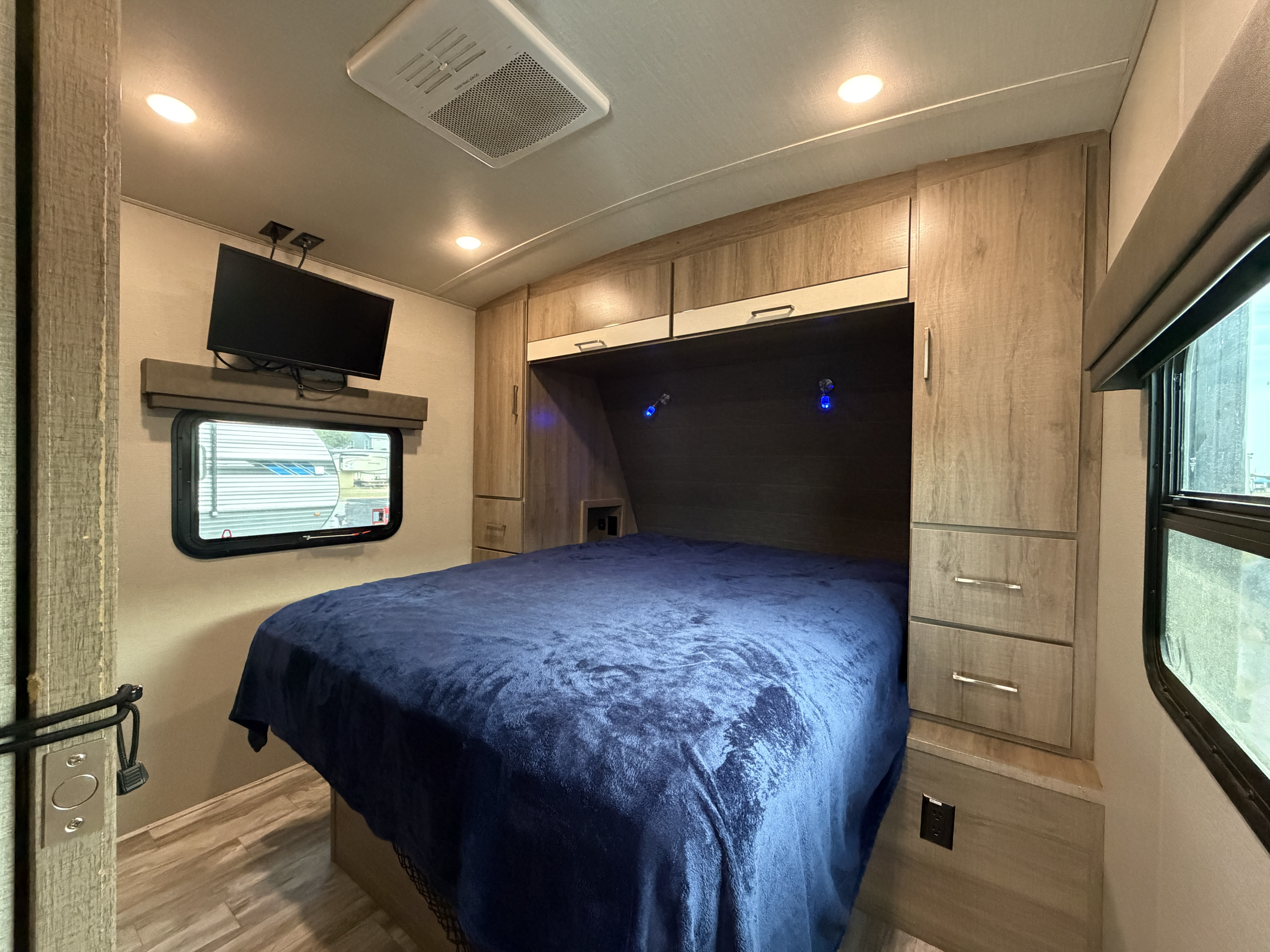 Modern RV rental bedroom with a cozy blue bed, mounted TV, AC, and ample storage. Perfect for your next adventure.. Grand Design Imagine 2023
