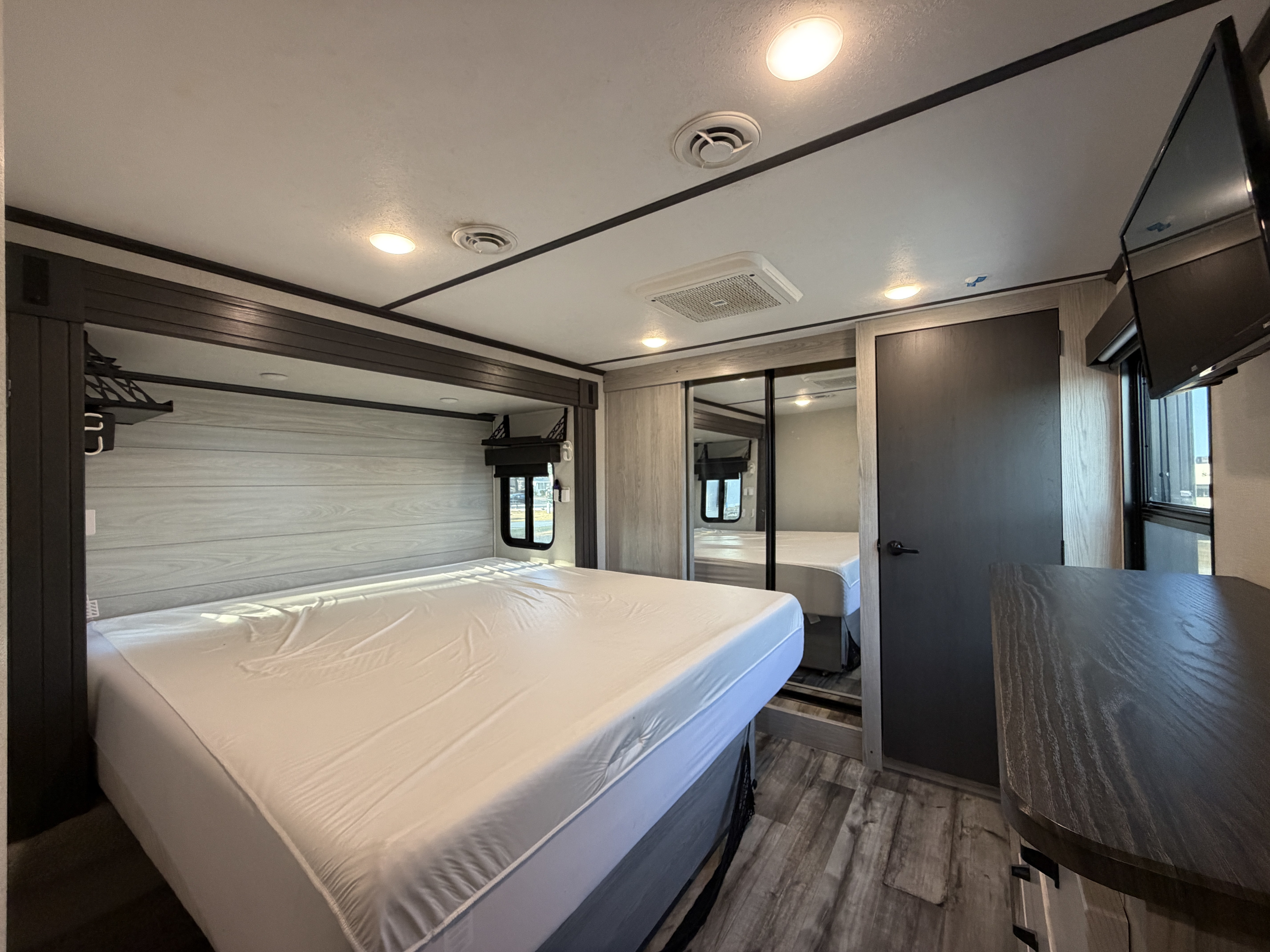 This RV rental features a modern bedroom with a large bed, mirrored closet, wall-mounted TV, and ample storage.. Keystone Montana High Country 2022