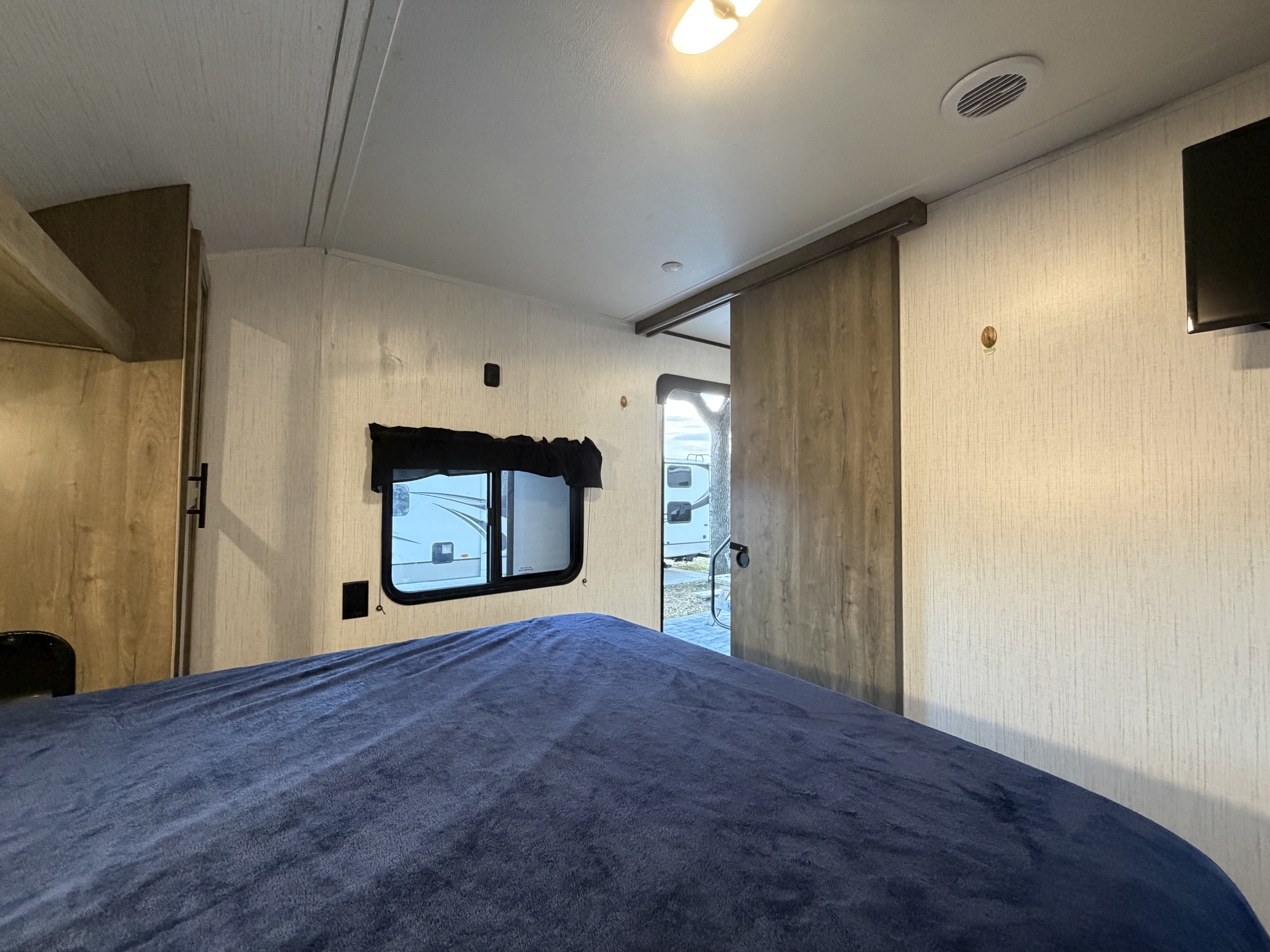 Interior of an RV rental bedroom with a comfy blue blanket on the bed, a window, and a sliding door.. Heartland Pioneer 2022