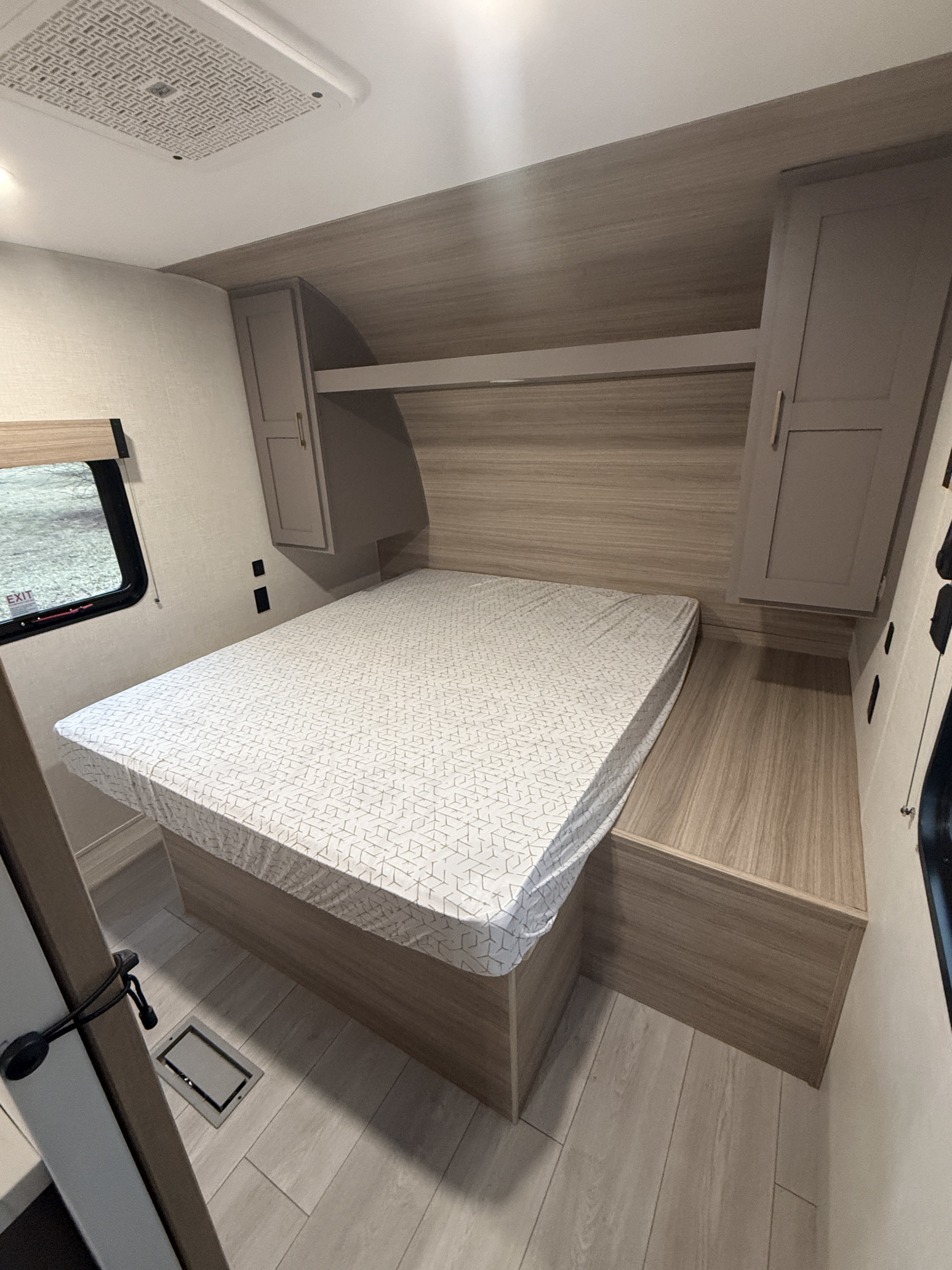 RV rental bedroom: a bed with patterned mattress, built-in storage, overhead cabinets, and a window. Features modern light wood decor.. Kz Sportsmen 332bhkse 2026