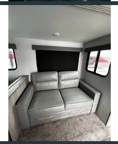 Plush gray Thomas Payne sleeper sofa in an RV rental, featuring a comfortable living space & carpeted floor for travel.. Riverside RV Intrepid 2023