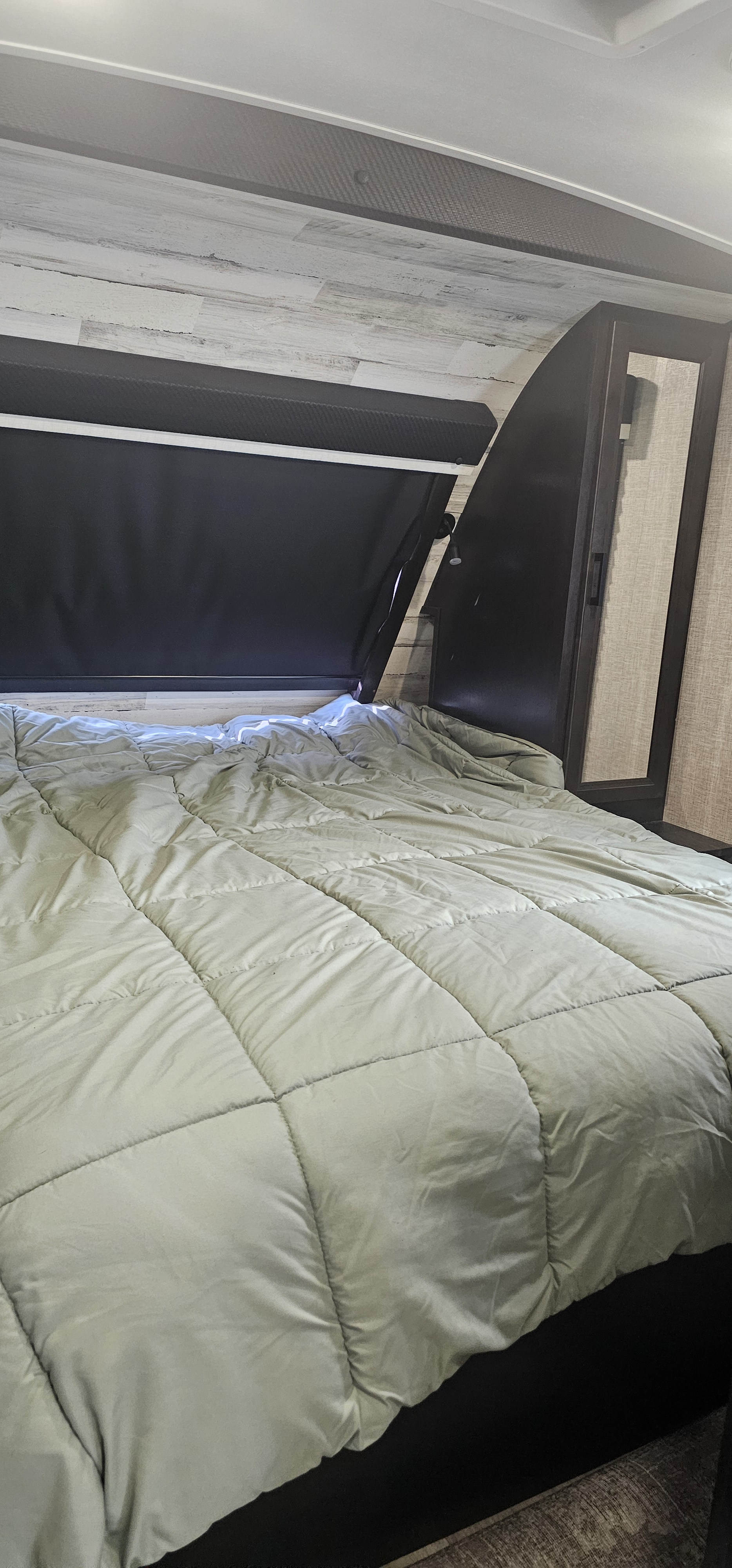 RV rental's cozy bedroom: a bed with light green quilted comforter, dark window blinds, and wood-look walls. Ready for rest.. Jayco White Hawk 2022