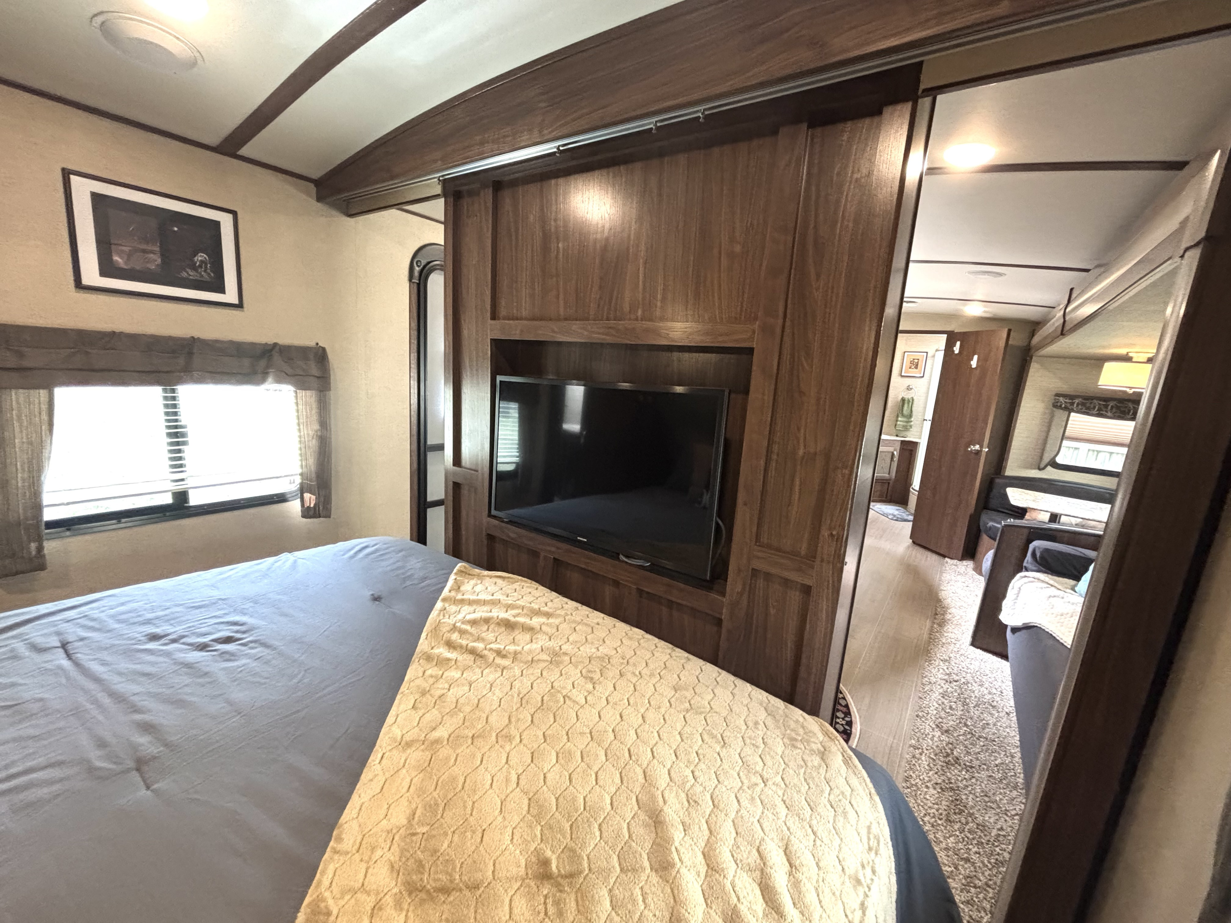 Cozy RV rental interior: bedroom with a blue bed and window, TV on a wooden sliding partition opening to the living area.. Dutchmen Aerolite 27RBSS 2017