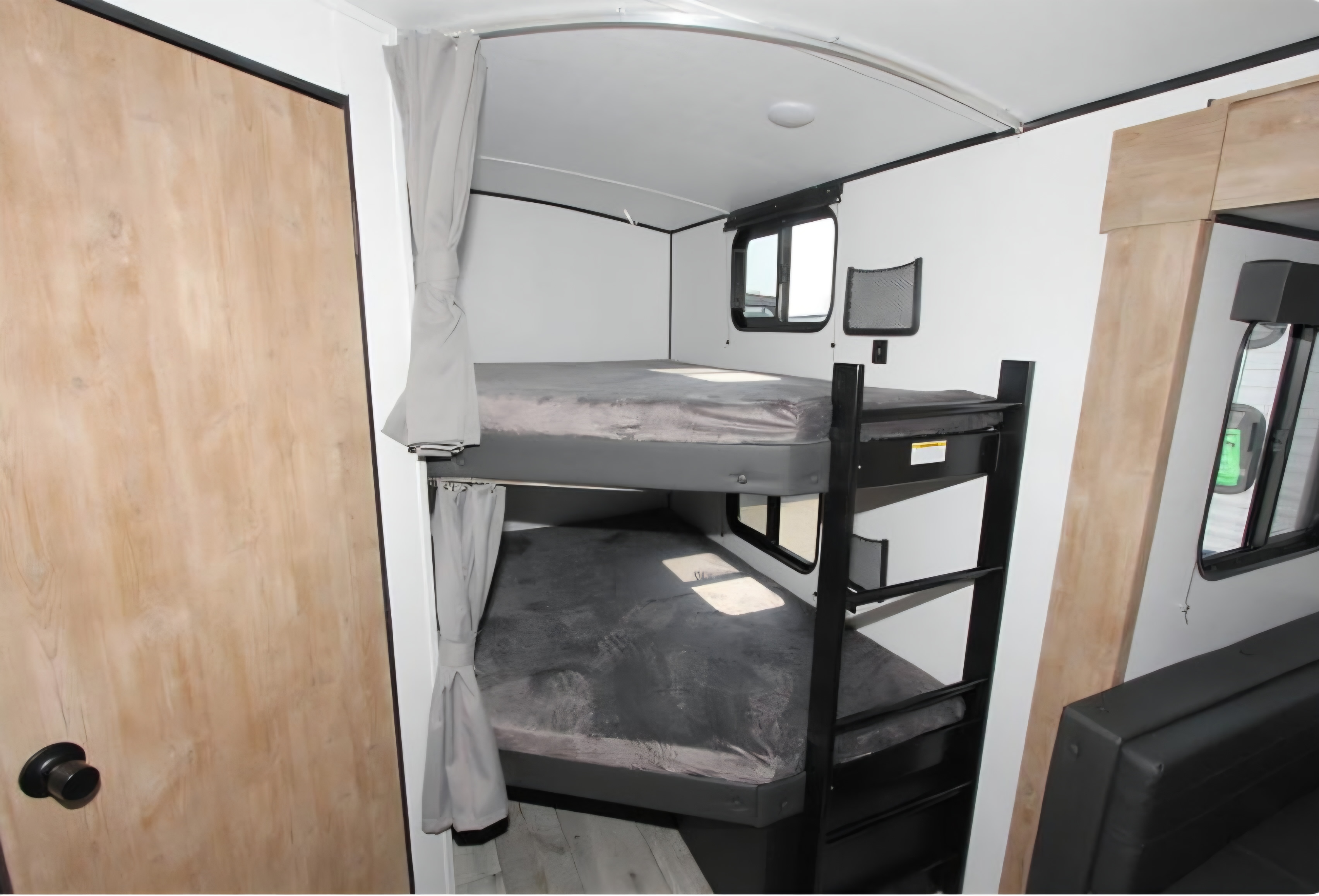 This RV rental interior features two cozy bunk beds with a ladder, a wooden door, and privacy curtains for comfortable sleeping.. Keystone RV Springdale 2023