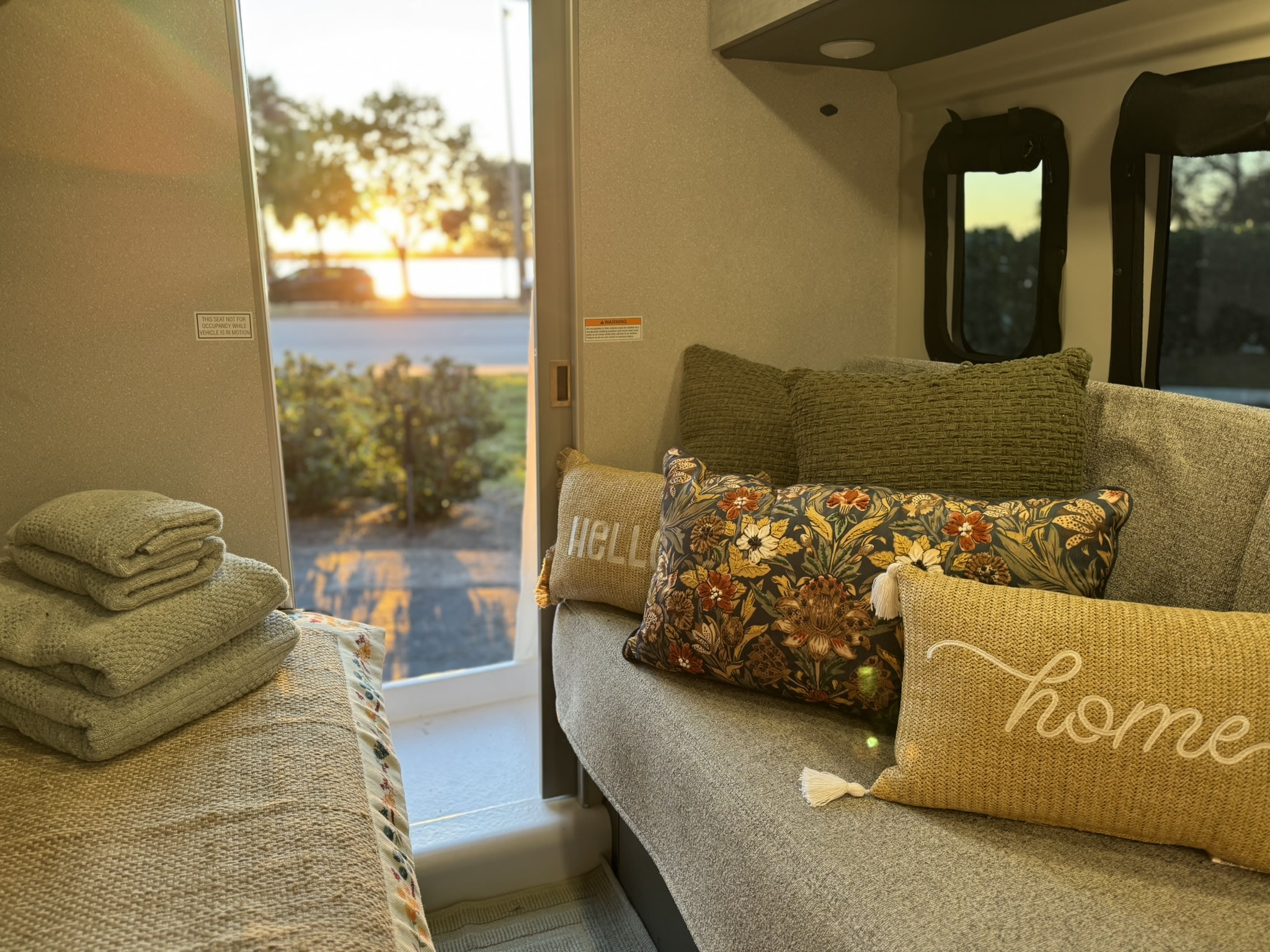 Cozy rv rental interior with decorative pillows, stacked towels, and an open door revealing a scenic sunset view.. Thor Twist 2025