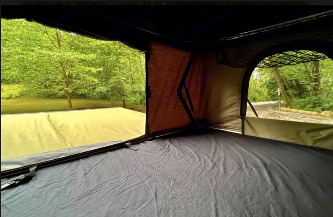 Cozy rooftop tent interior with dark bedding, mesh storage, and panoramic views of lush green trees, perfect for an RV rental adventure.. Dodge B Van 2008