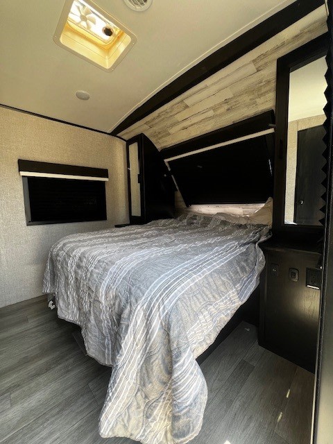 Cozy RV rental bedroom with a gray striped bed, wood-look floor, and overhead fan.. Jayco White Hawk 2022