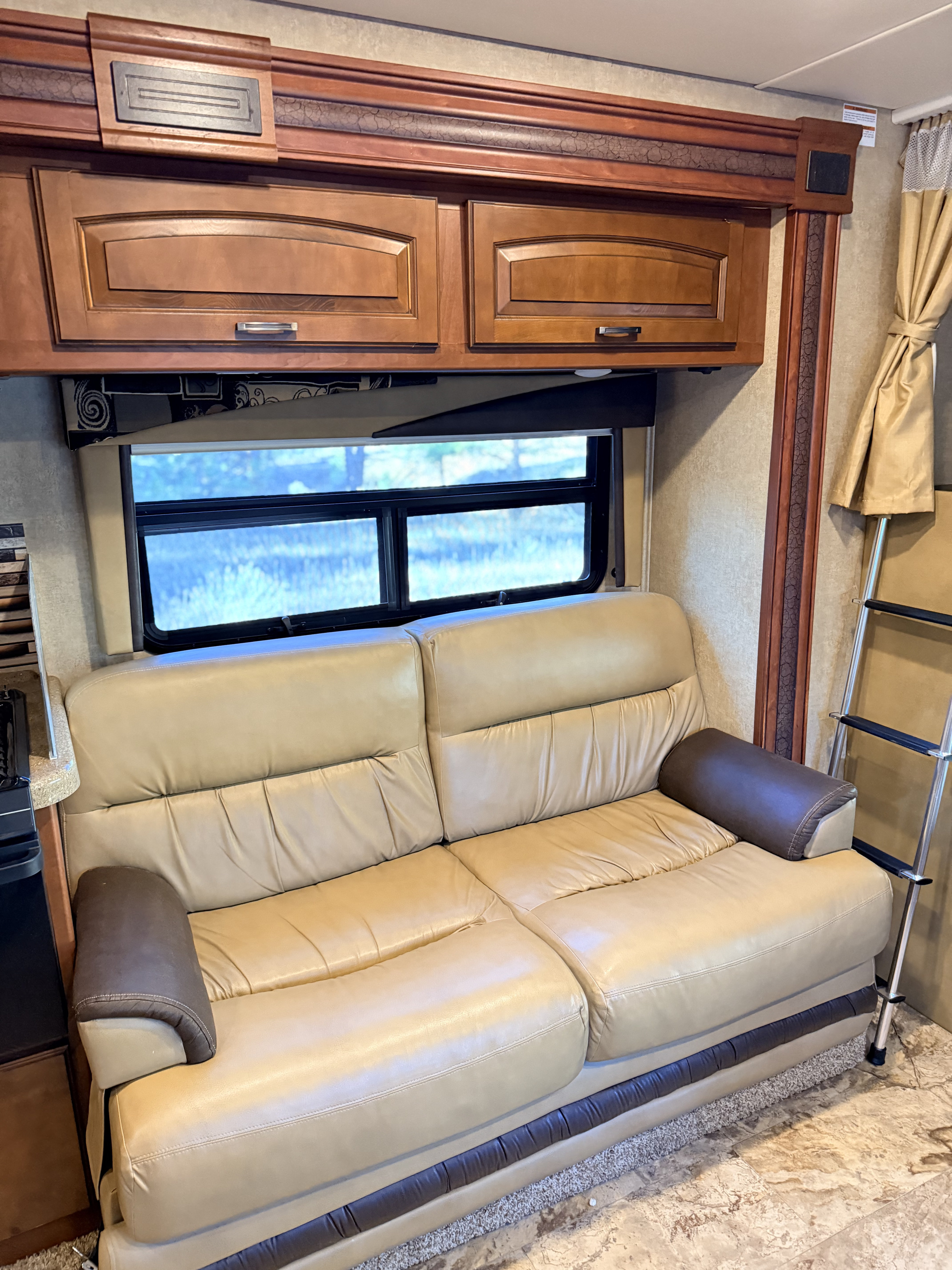 RV rental interior: a comfy beige leather sofa, rich wooden cabinets, and a scenic window create a cozy living space.. Jayco Greyhawk 2015