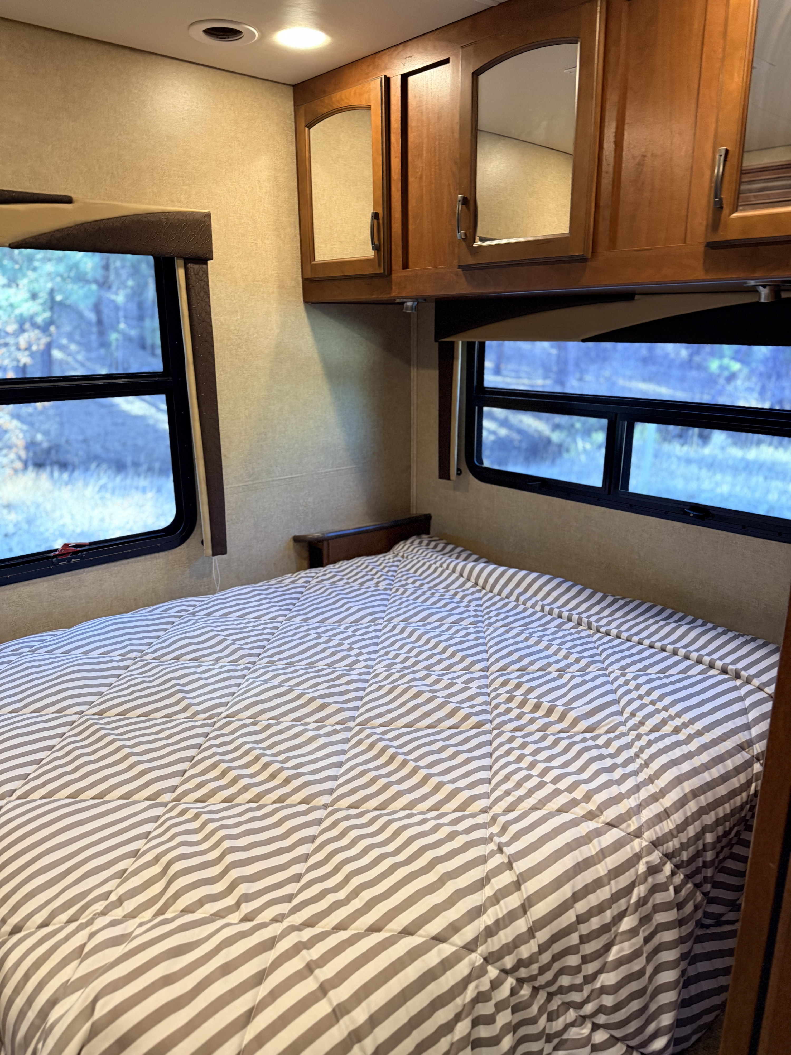 Cozy RV rental bedroom with striped bed, scenic windows, and storage cabinets, perfect for your next adventure.. Jayco Greyhawk 2015