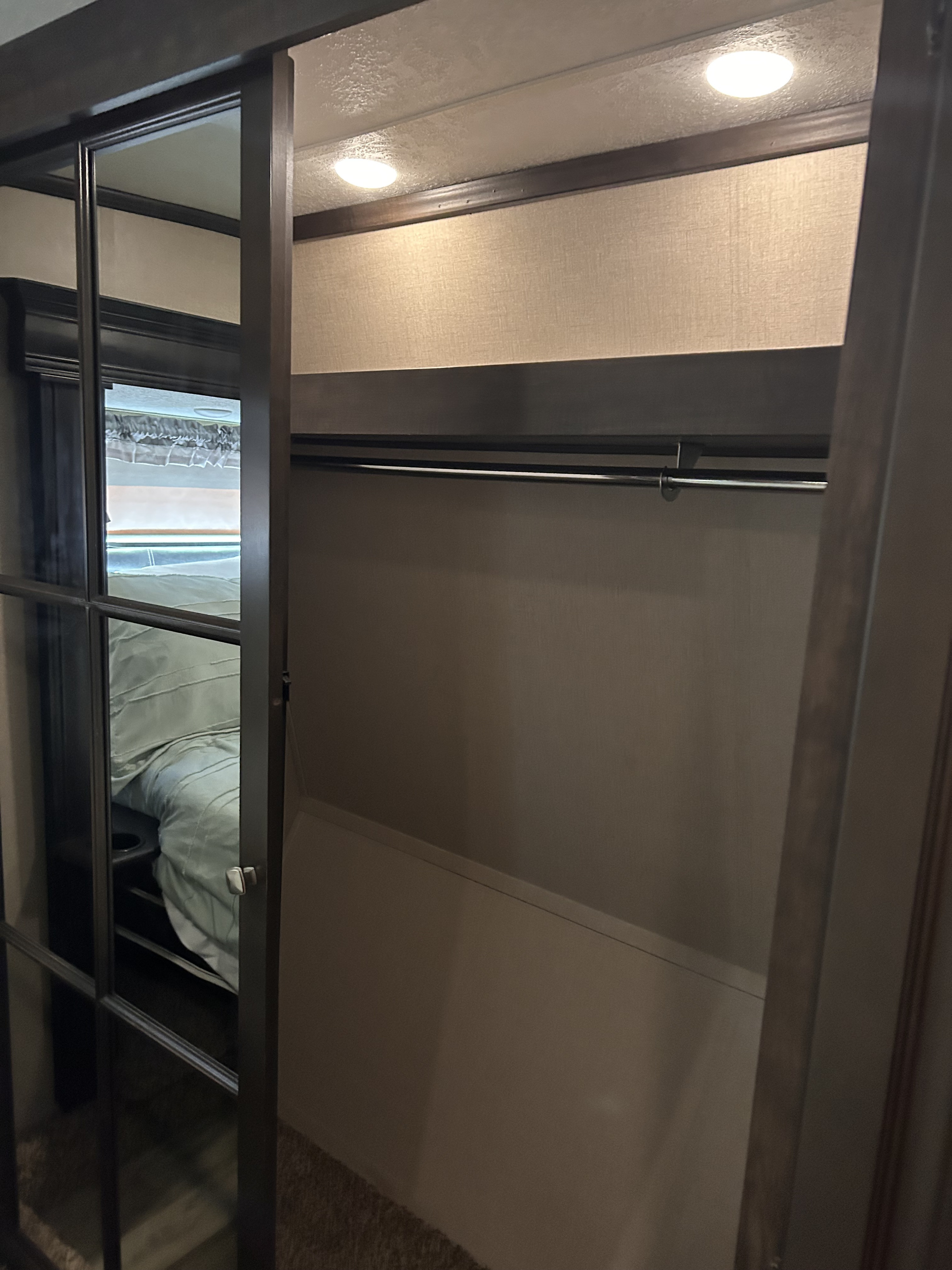 This RV rental features a modern closet with a hanging rod, recessed lighting, and a reflective glass door showing the bedroom.. Coachmen Brookstone 2021