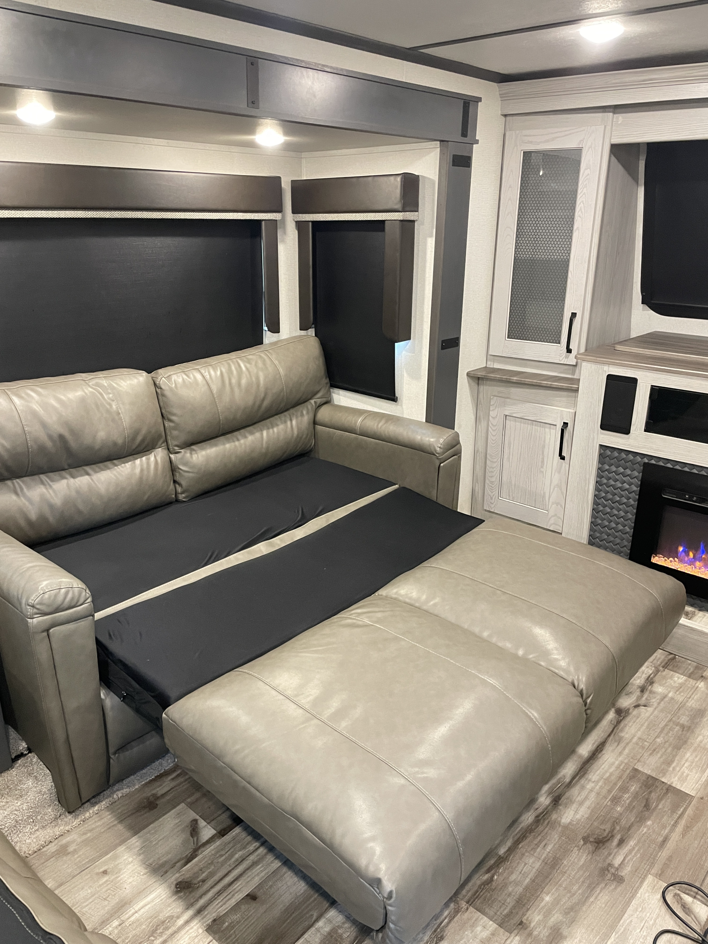 RV rental interior featuring a partially extended gray leather pull-out couch, electric fireplace, light wood cabinets, and black shades.. Keystone RV Montana High Country 2022