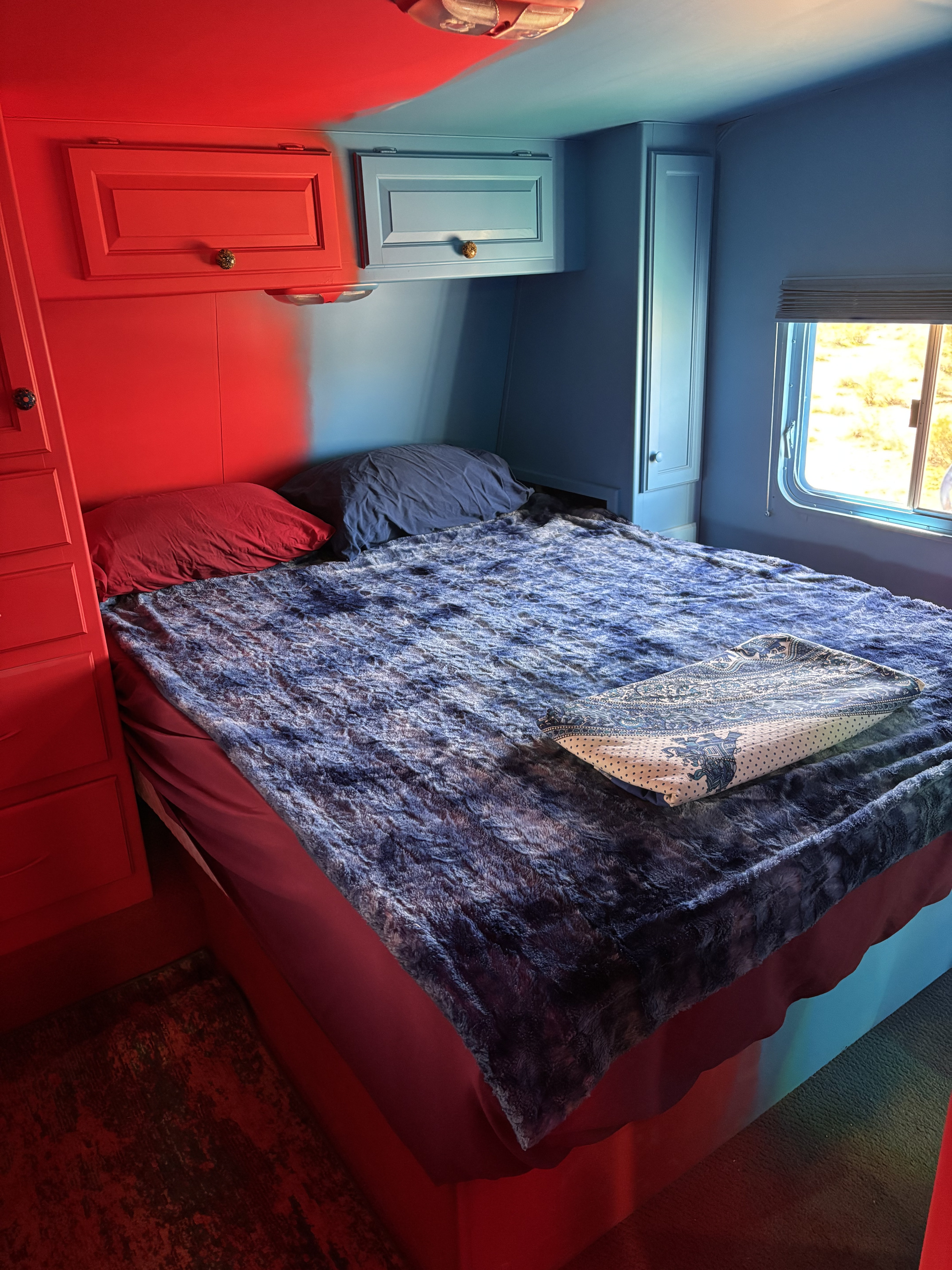 Vibrant red and blue two-tone RV rental bedroom interior with bed, pillows, and cabinets.. Keystone Raptor 2026