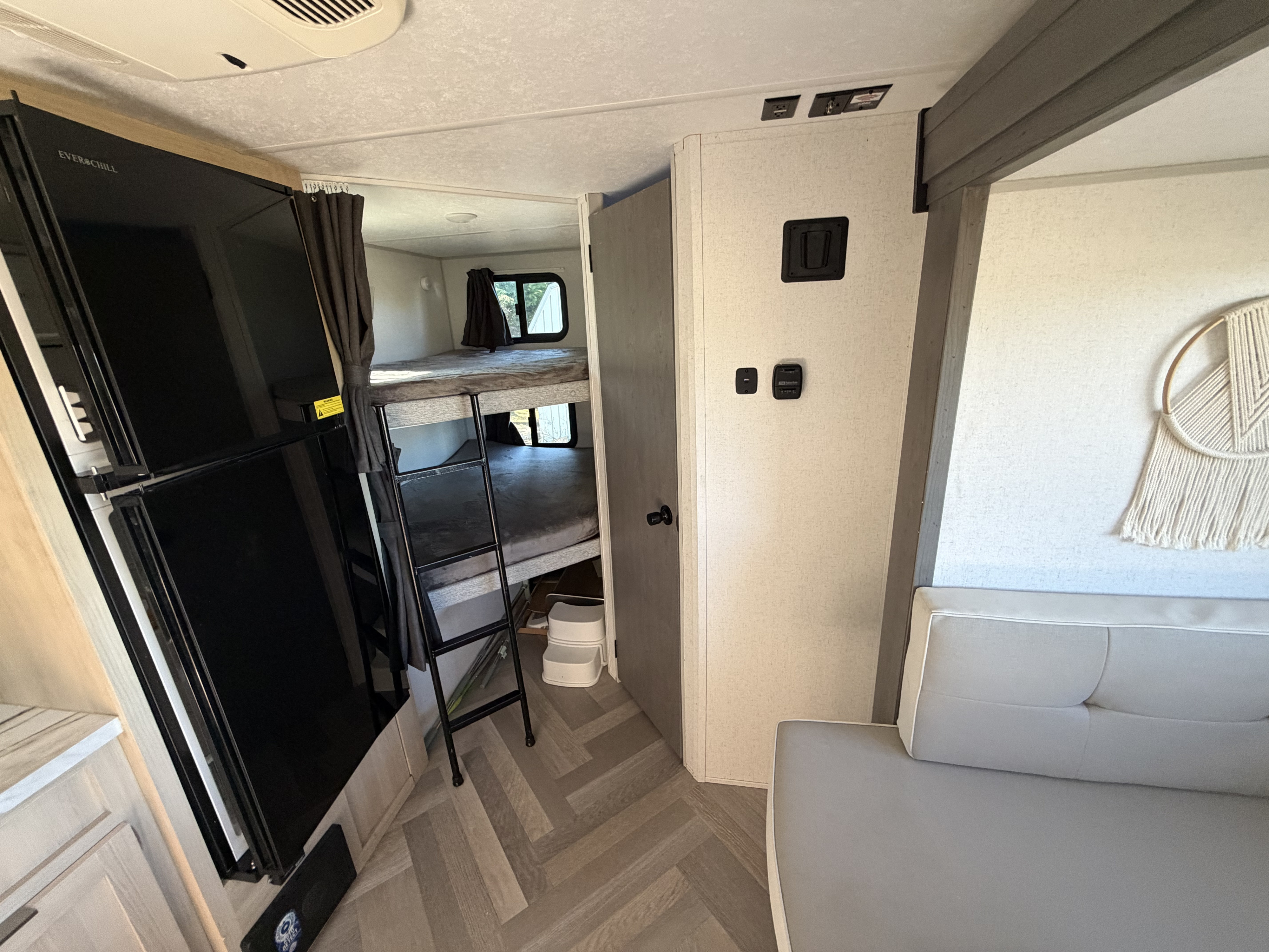 View of an rv rental's interior, showcasing bunk beds with a ladder, a black refrigerator, and part of a light gray sofa.. Forest River Wildwood FSX 2023