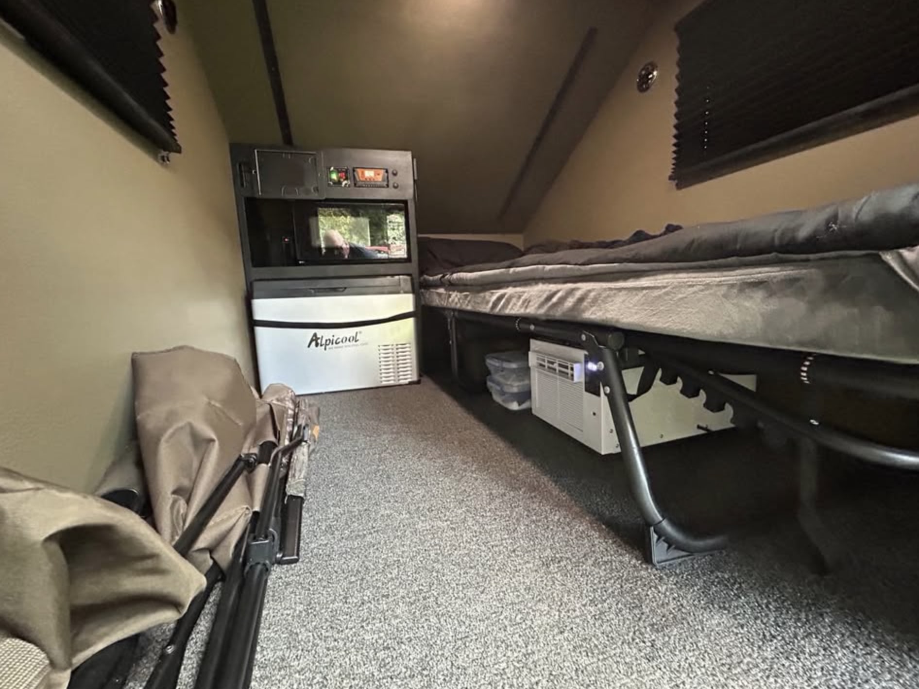 Explore this compact RV rental interior featuring a bed, portable fridge, microwave, AC, and folded camping chairs.. Tusca Hitchhiker 2024