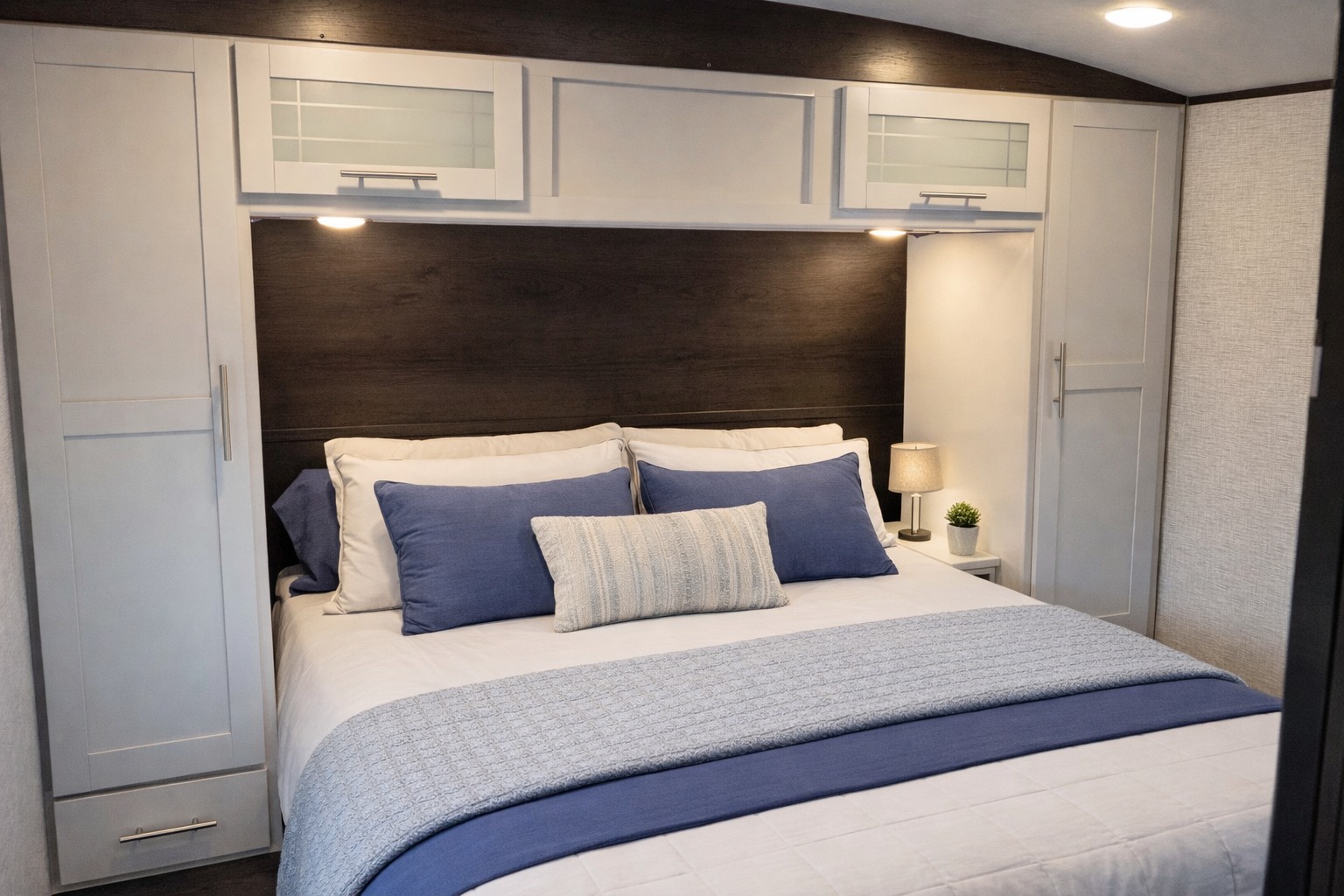Modern RV rental bedroom: blue and white bedding, dark wood headboard, built-in storage, and soft lighting for a cozy stay.. Keystone RV Bullet Premier Ultra 2021