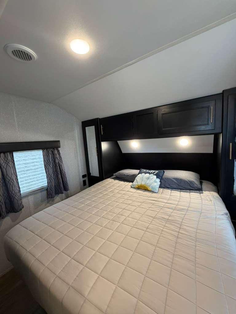 Experience comfort in this RV rental bedroom: quilted bed, overhead cabinets, and soft lighting. Your mobile retreat awaits.. Forest River Wolf Pup 2021