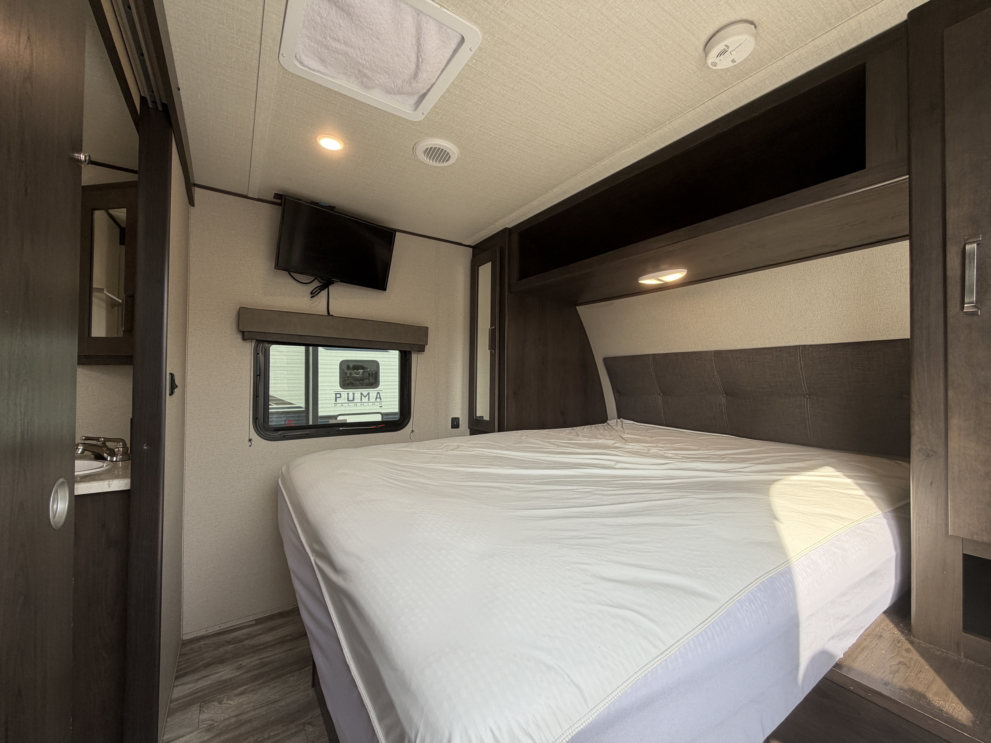 RV rental bedroom with a bed, TV, window, and partially visible sink area, offering a compact, comfortable stay.. Grand Design Transcend 265BH 2022