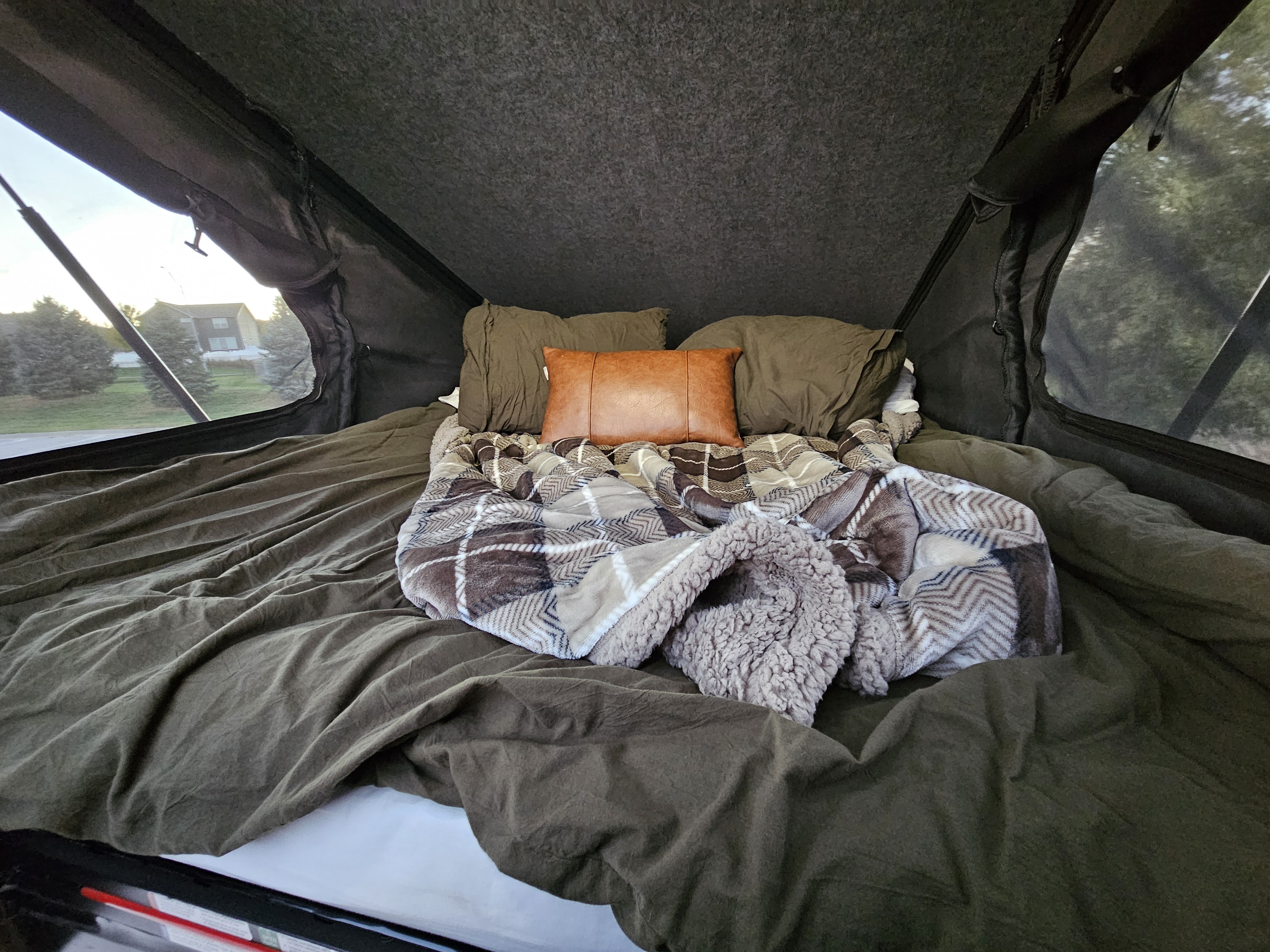 A cozy RV rental bed setup with olive green bedding, a warm plaid sherpa blanket, and a brown accent pillow inside a pop-up tent.. Mercedes-Benz Sprinter 2025