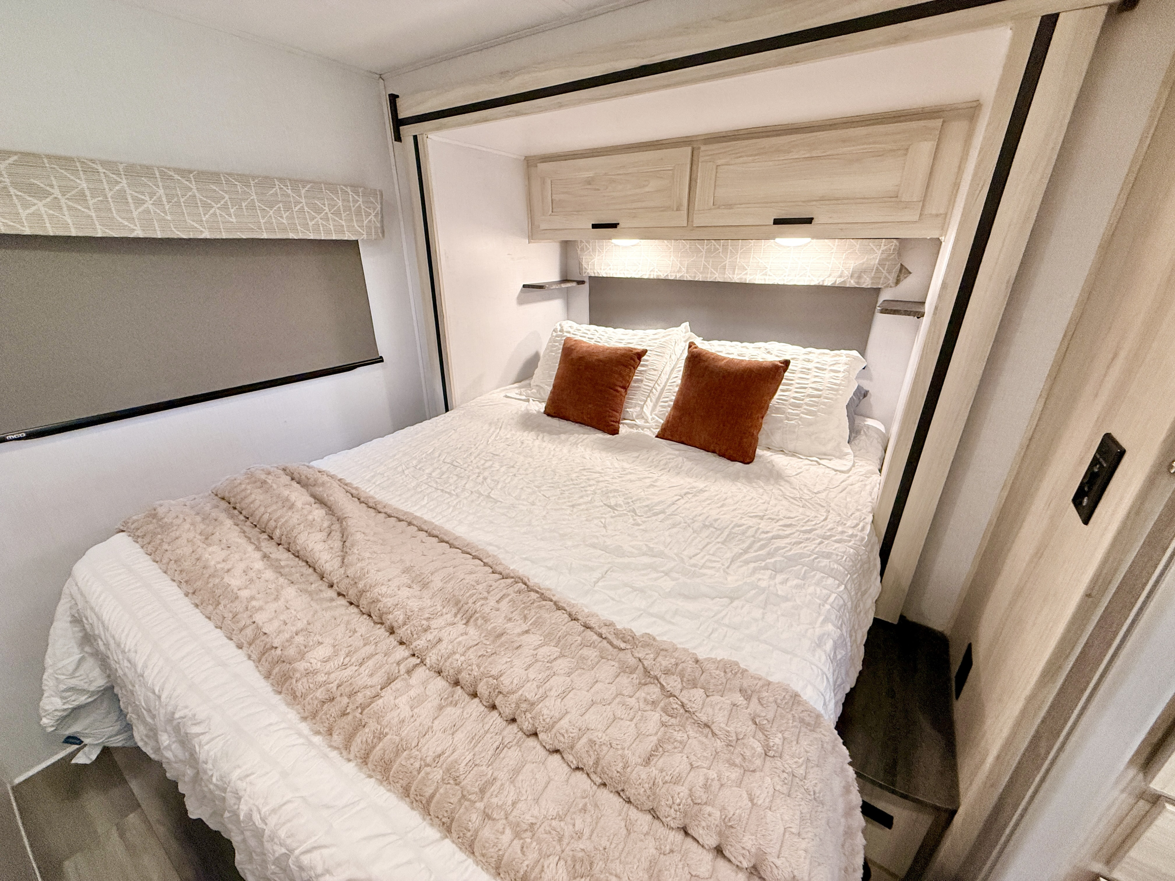 Modern RV rental bedroom with a cozy bed, white linens, and soft textured throw. Features overhead cabinets & ambient lighting.. Forest River, Inc. 2250SLE 2023