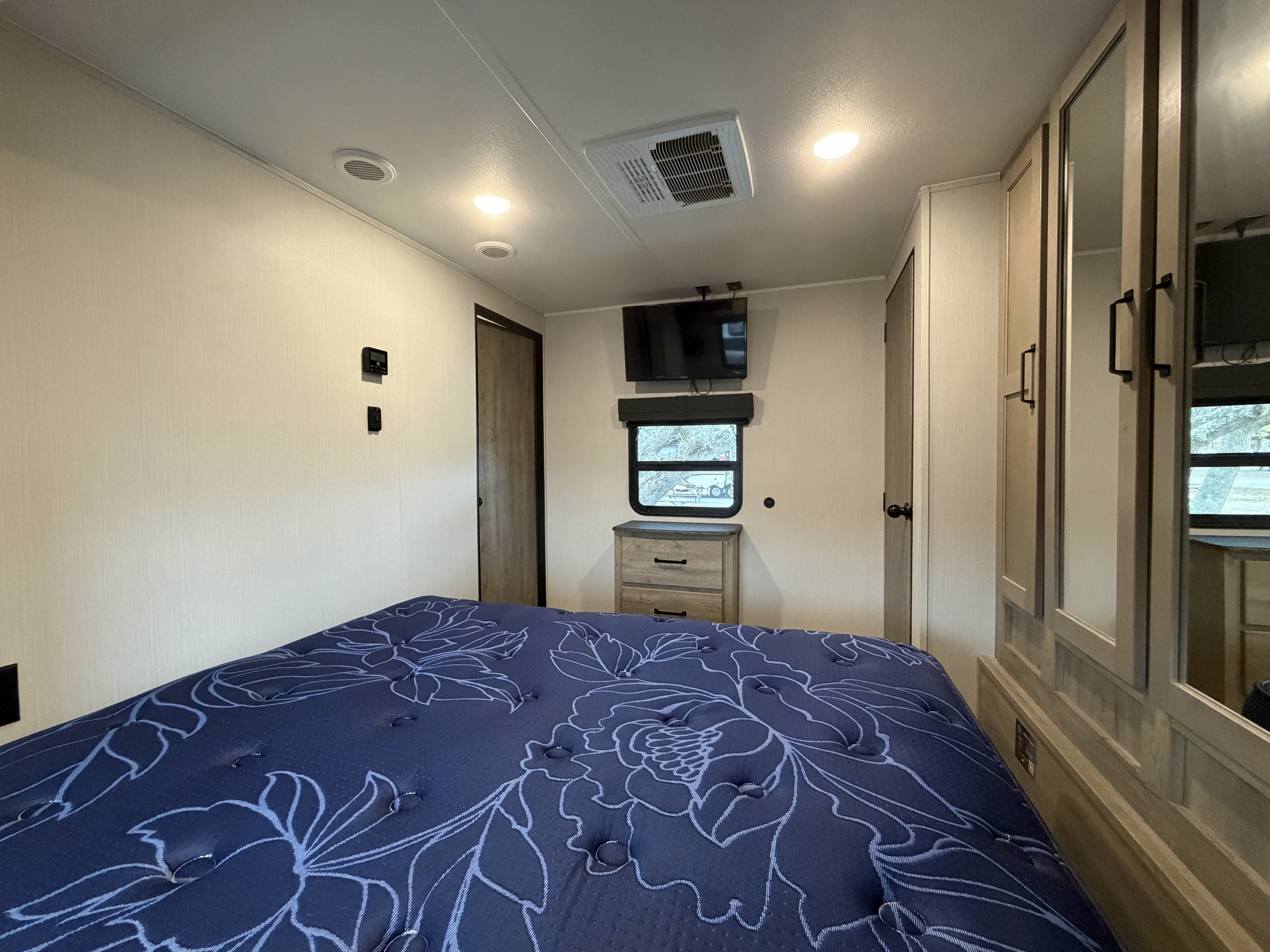 RV rental bedroom: Blue floral bed, wall-mounted TV, window, dresser, & closet. Well-appointed for travel comfort.. Forest River Puma 2024