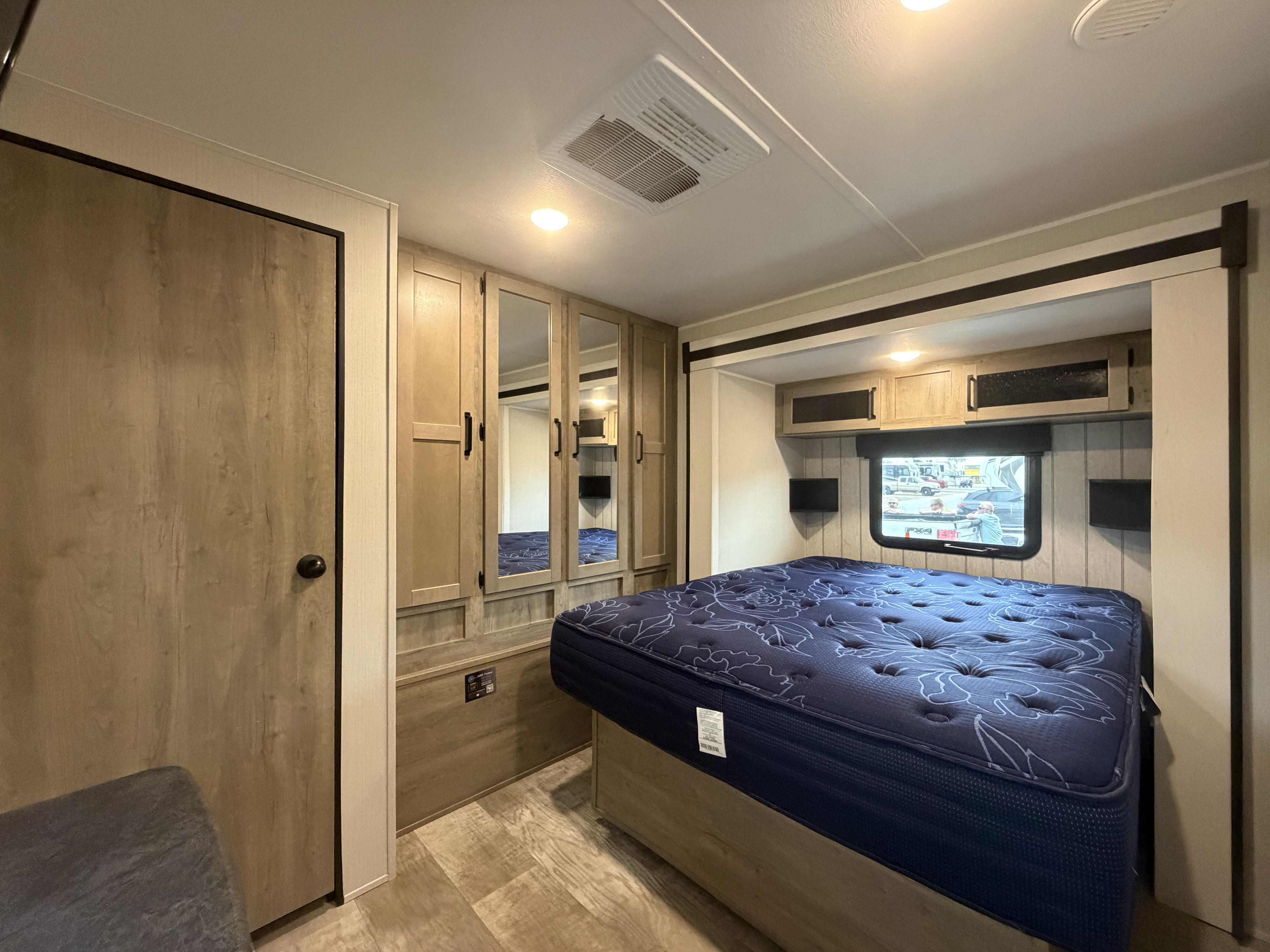 RV rental bedroom with blue floral mattress, ample wood cabinetry, and a window. Cozy interior for your travels.. Forest River Puma 2024